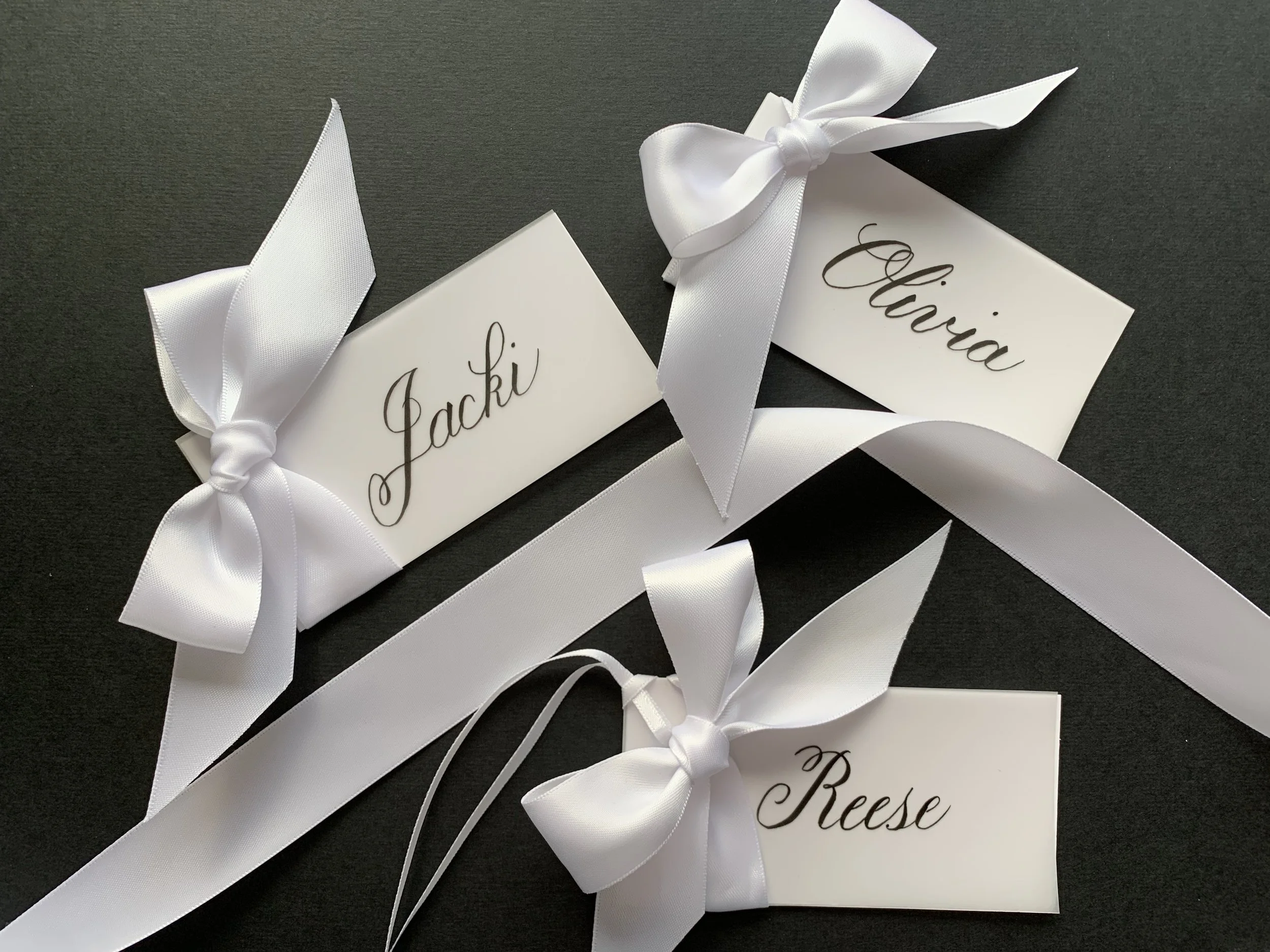 Calligraphy gift tag with white satin ribbon and bow with another ribbon for attaching to gift.