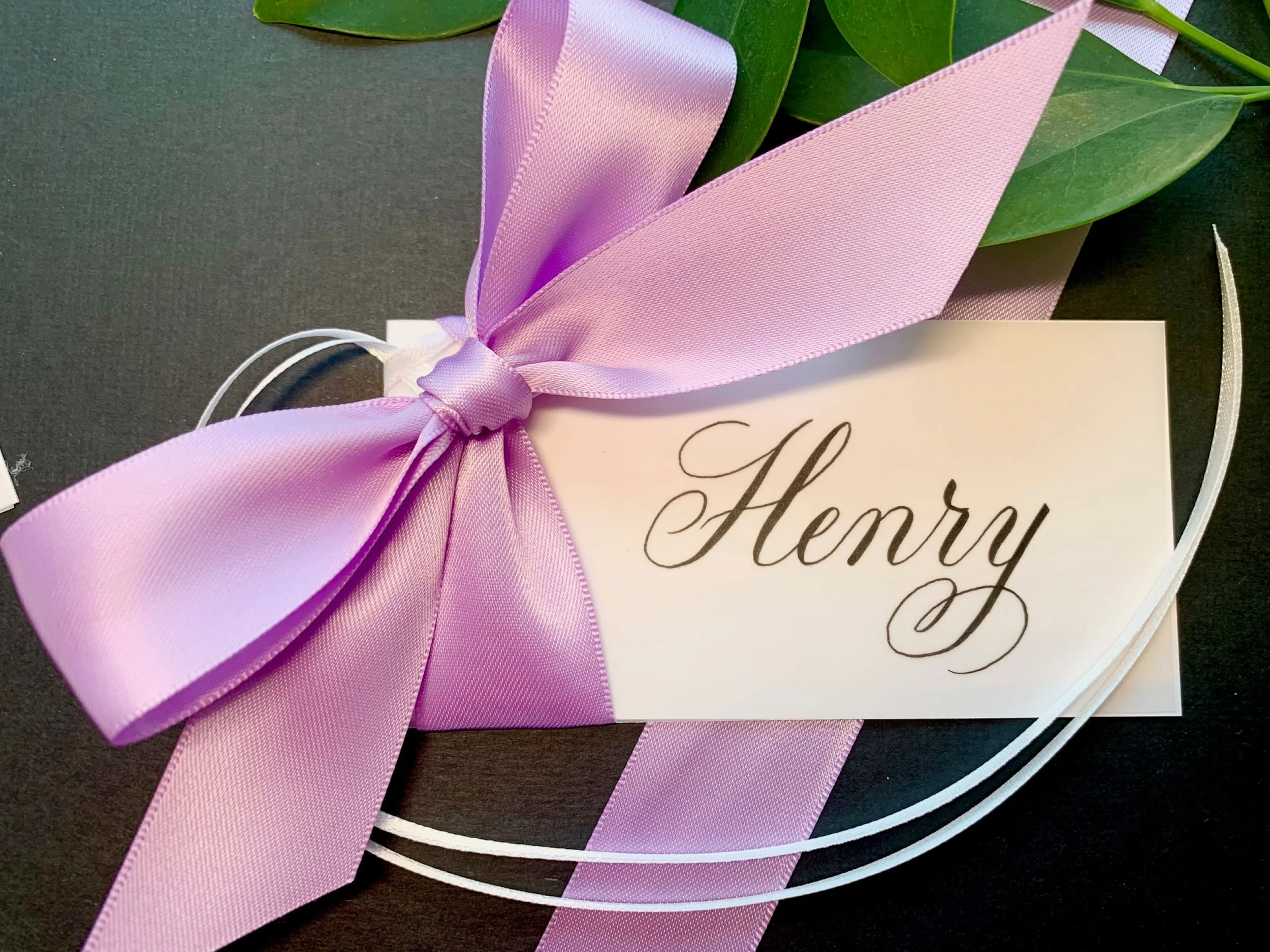 Calligraphy gift tag with lavender satin ribbon and bow showing white ribbon for tying to gift.