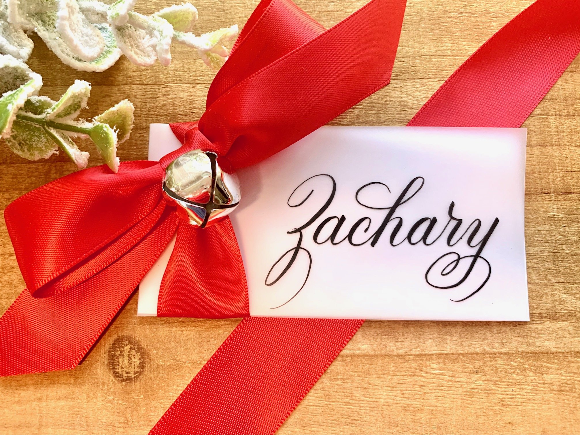 Calligraphy Christmas place card with handwritten first name and decorated with jingle bell and red satin bow