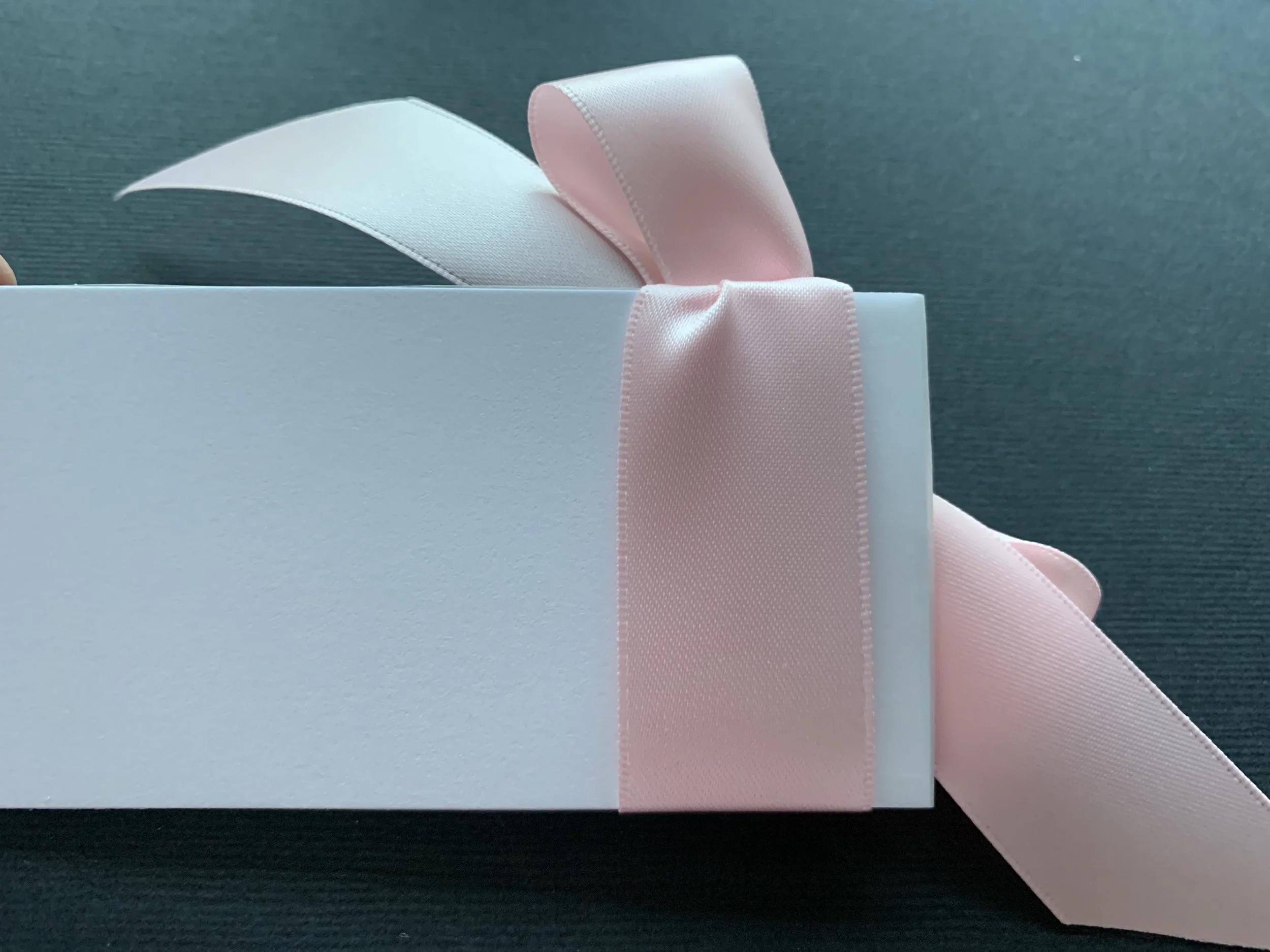 Back of white calligraphy place card showing light pink ribbon attached