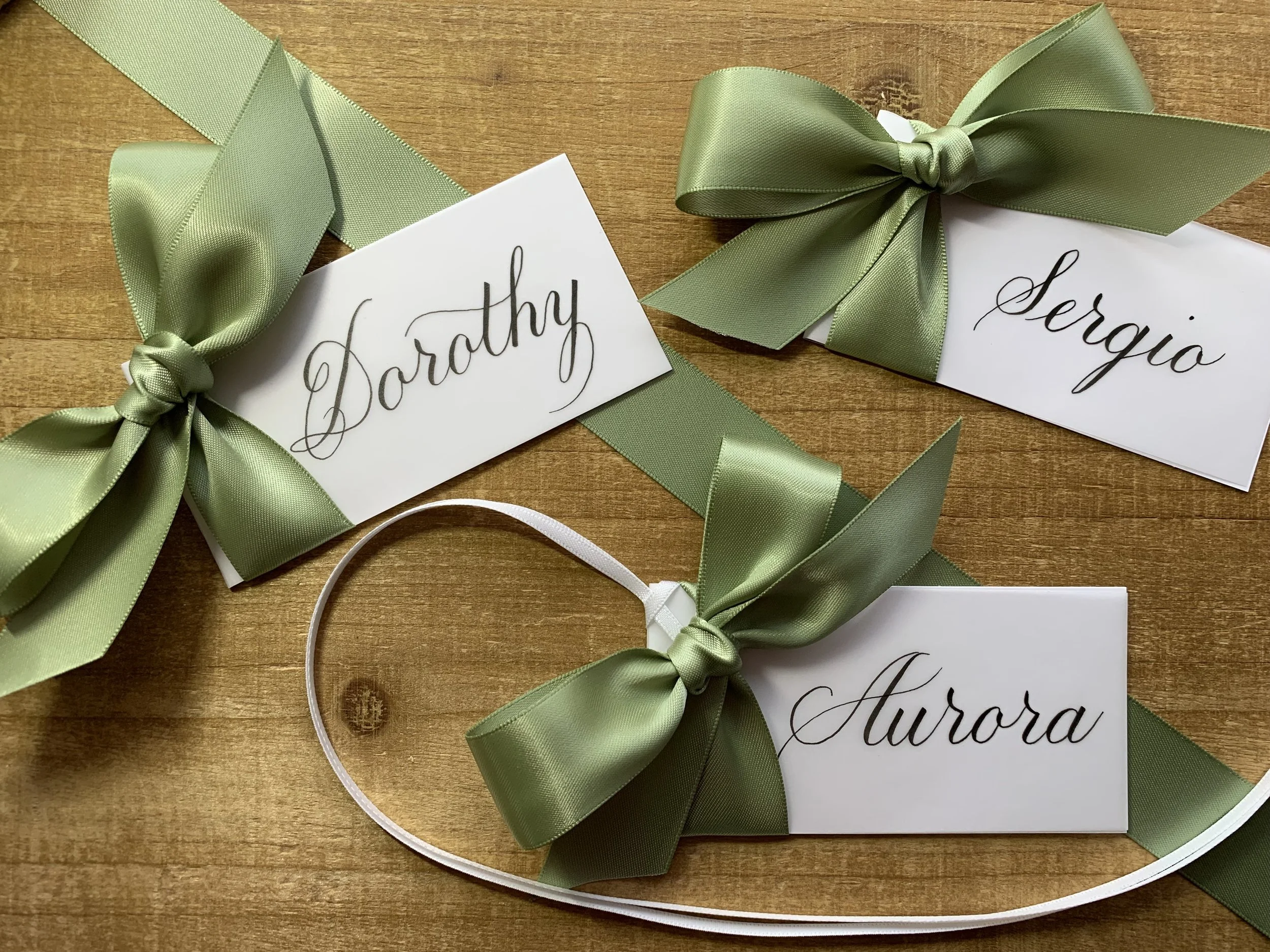 Calligraphy place cards and gift tag decorated with sage green ribbon and bow