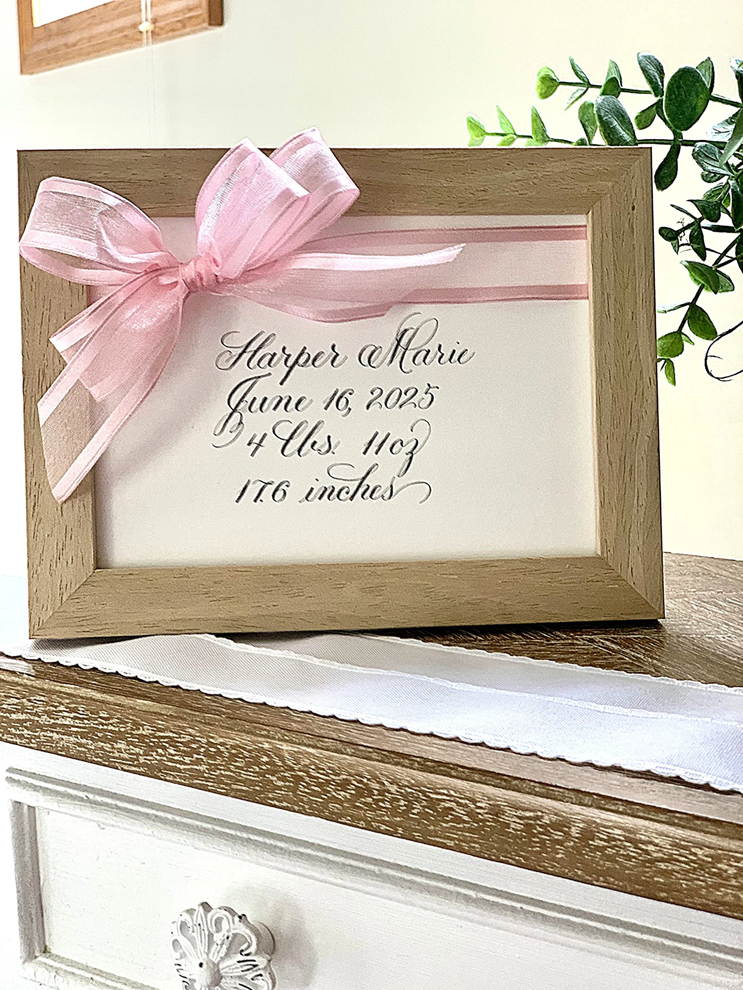 Baby announcement gift of framed calligraphy baby name and weight decorated with pink ribbon bow.