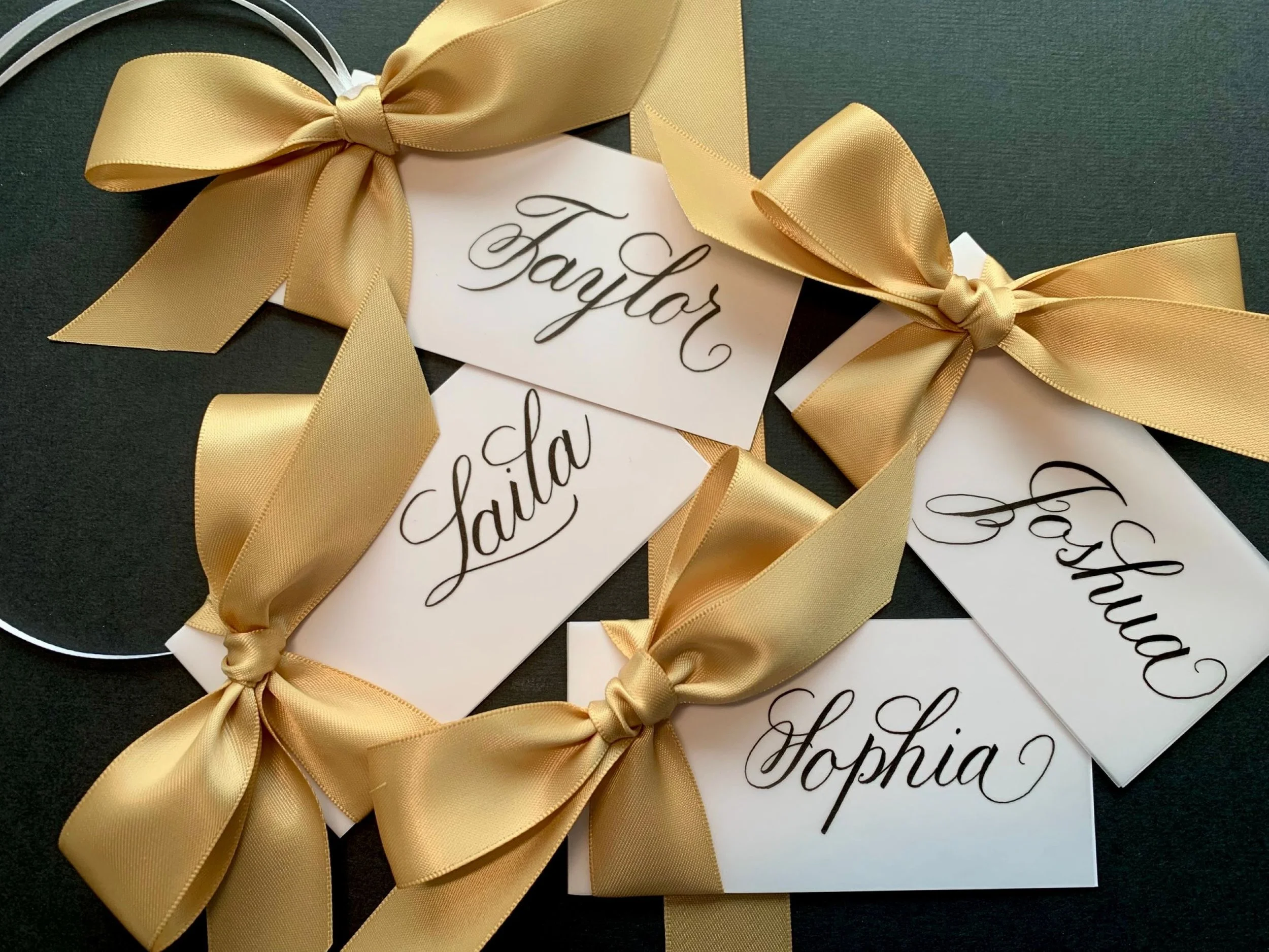 Gold ribbon and bow attached to handwritten calligraphy white place cards