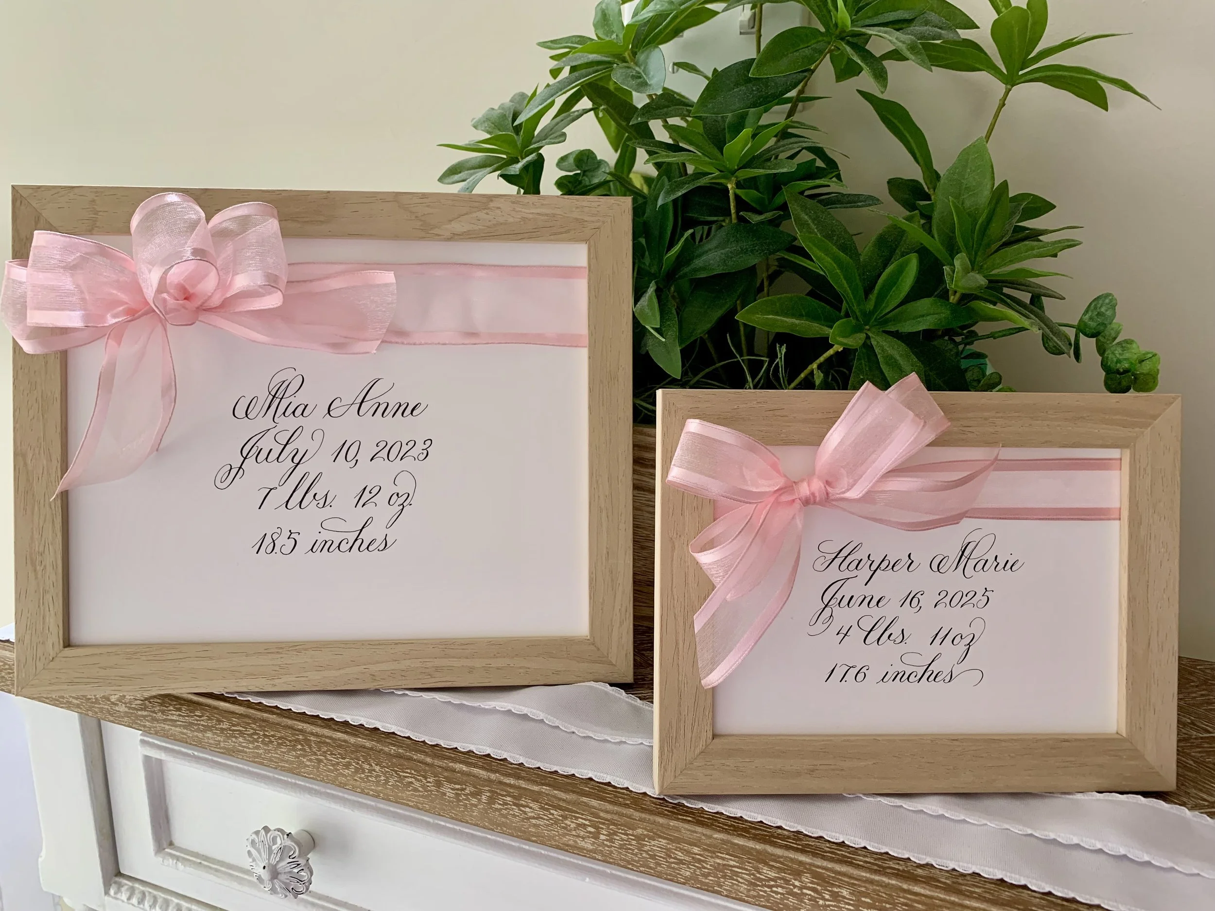 Pink bow baby name sign written calligraphy in wooden frame for new baby gift or nursery decor.
