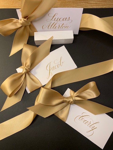 Calligraphy gold ink and gold satin ribbon place cards for wedding.