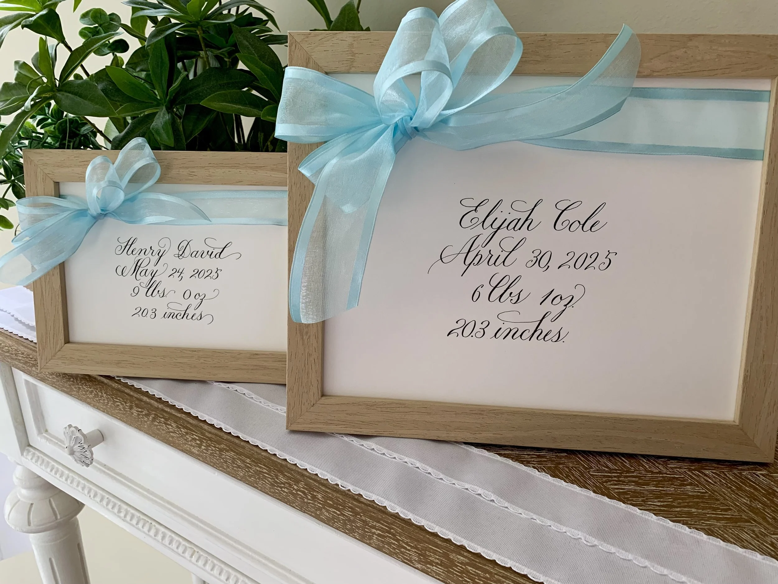 Blue bow baby name sign written in calligraphy in wooden frame for new baby gift.