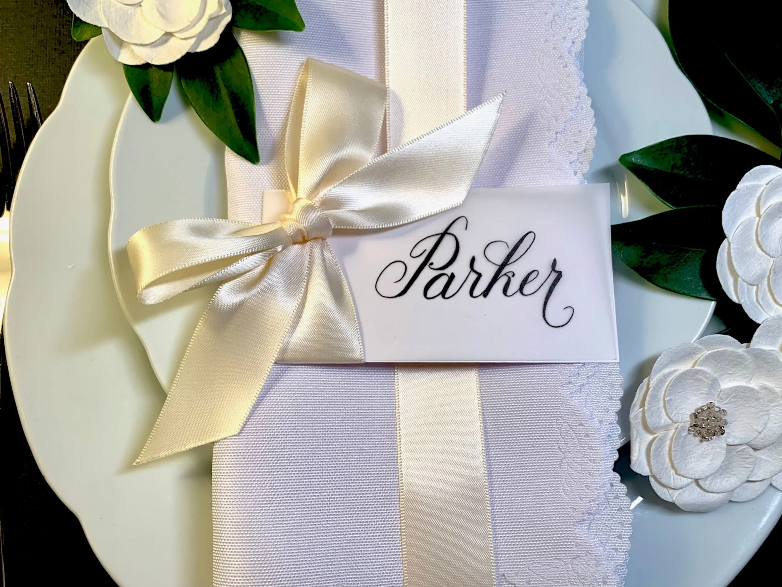 Cream-colored ribbon and bow on calligraphy place card laying flat at place setting on table
