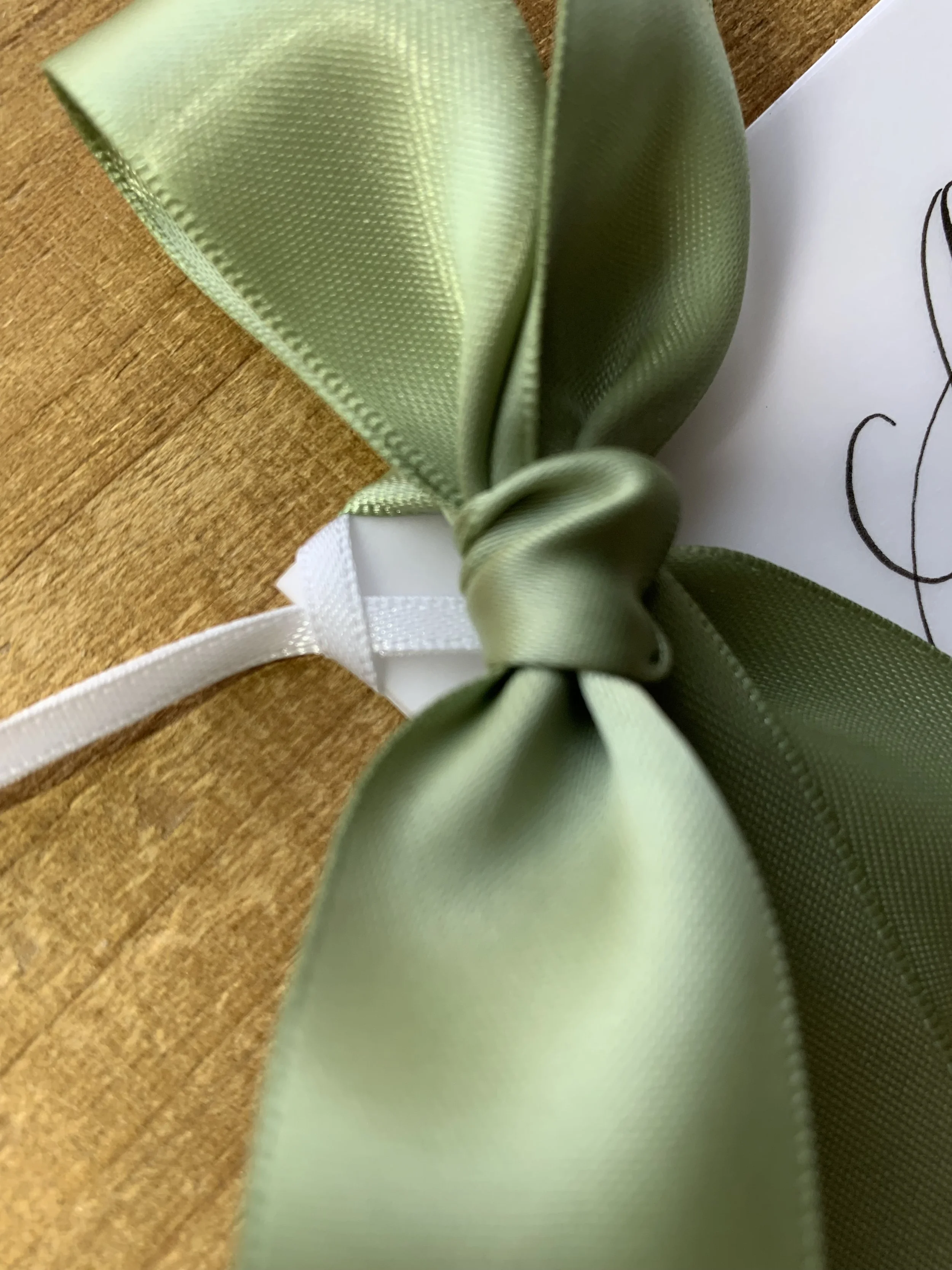 close up of sage green ribbon and white ribbon tie on calligraphy gift tag