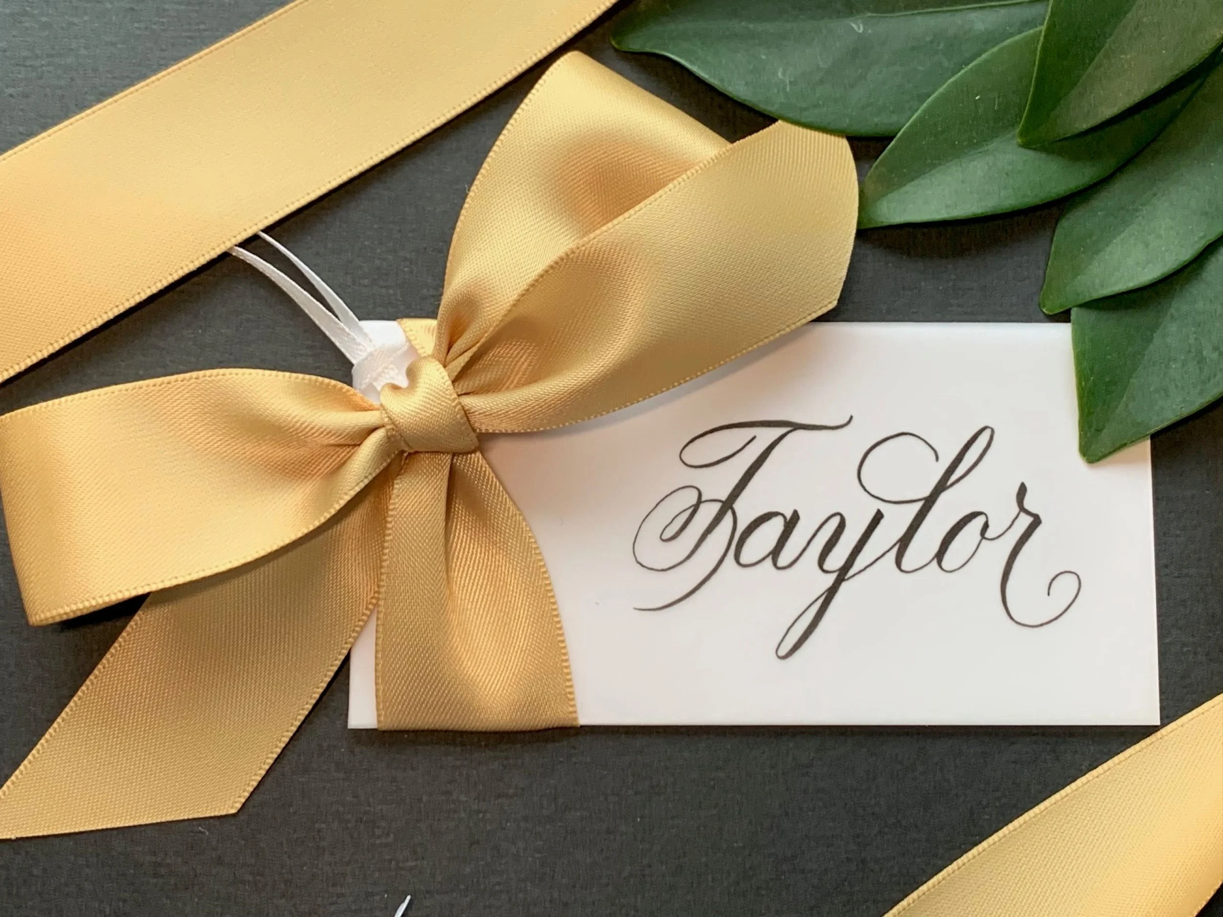 Gold ribbon place card and bow personalized with custom calligraphy.