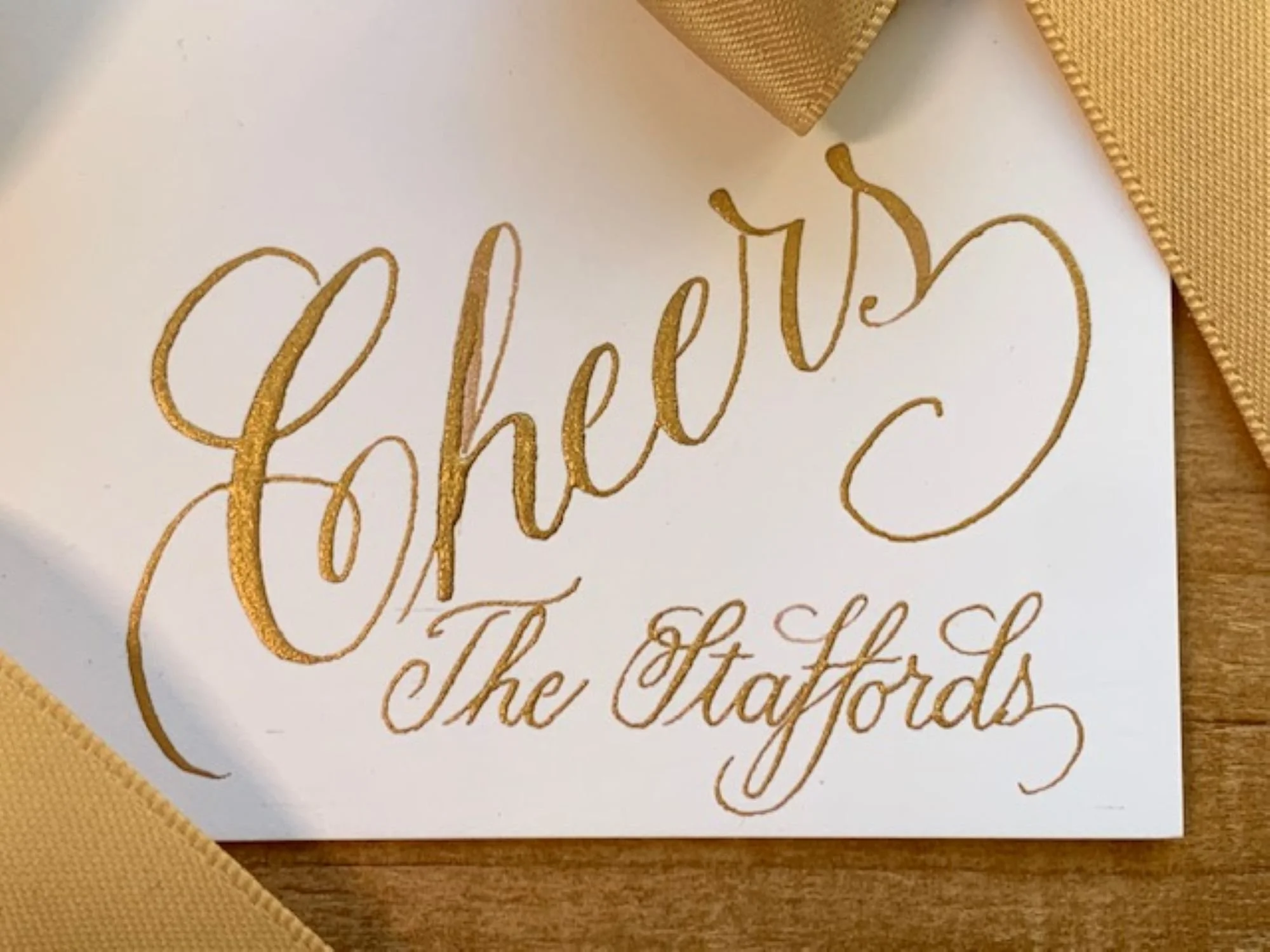 Close-up of custom gold calligraphy on wine bottle gift tag with gold satin bow