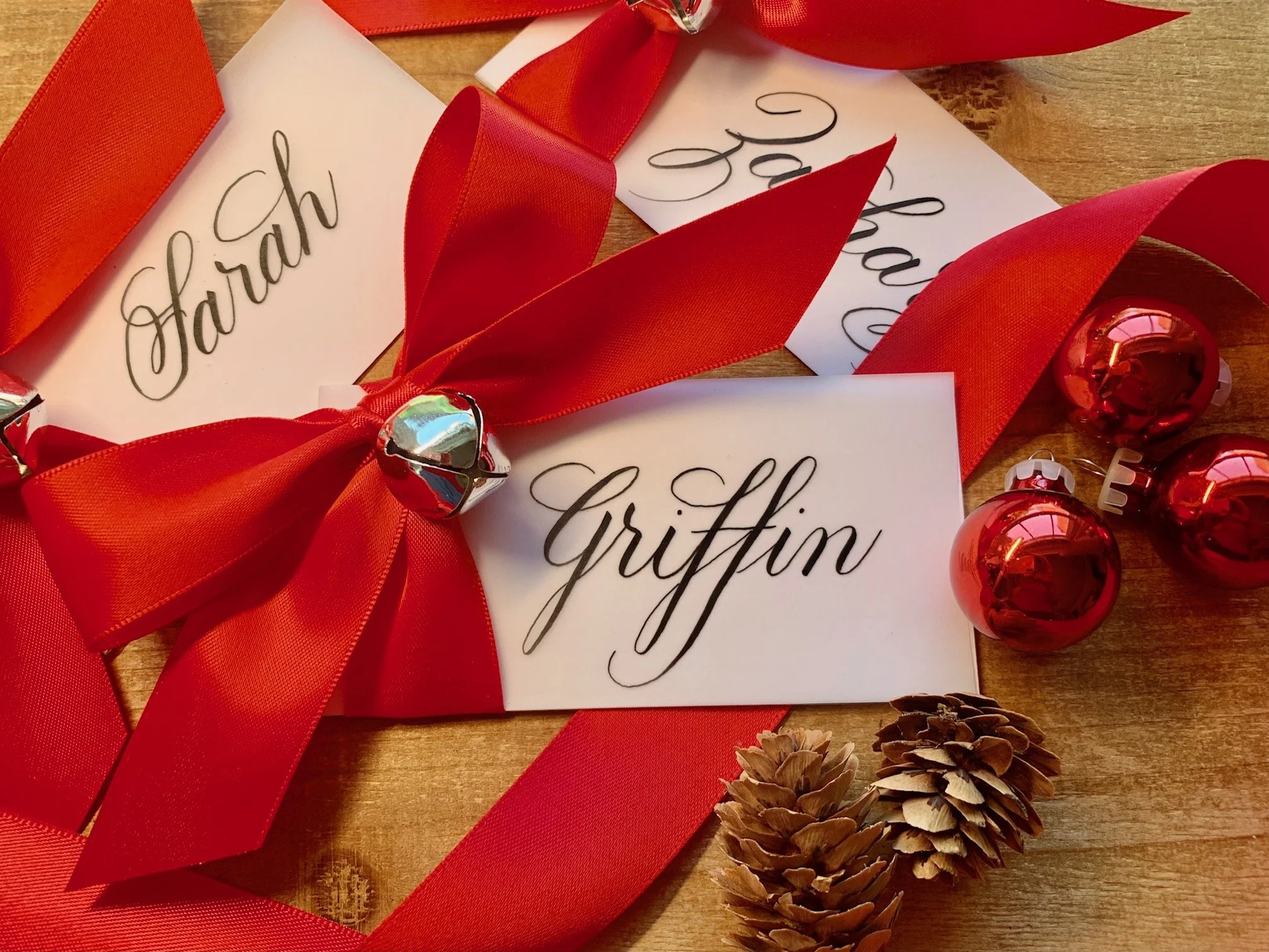 Christmas jingle bell place cards with red satin ribbon and personalized with handwritten calligraphy