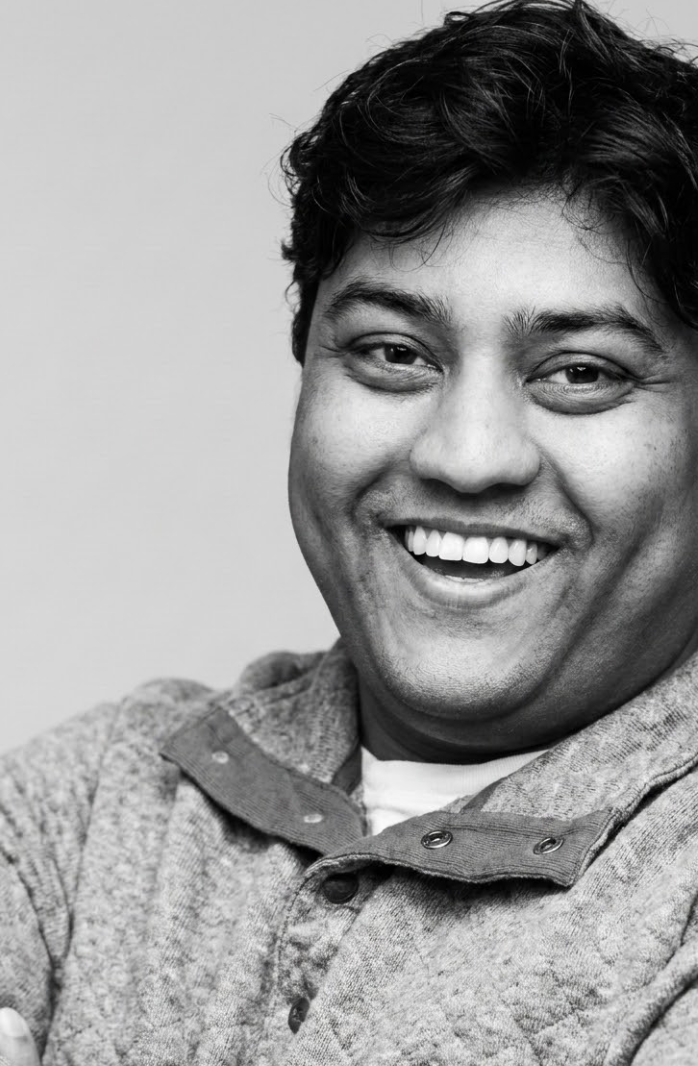 Black and white photo of a smiling man with short, dark hair, wearing a collared shirt and a jacket.