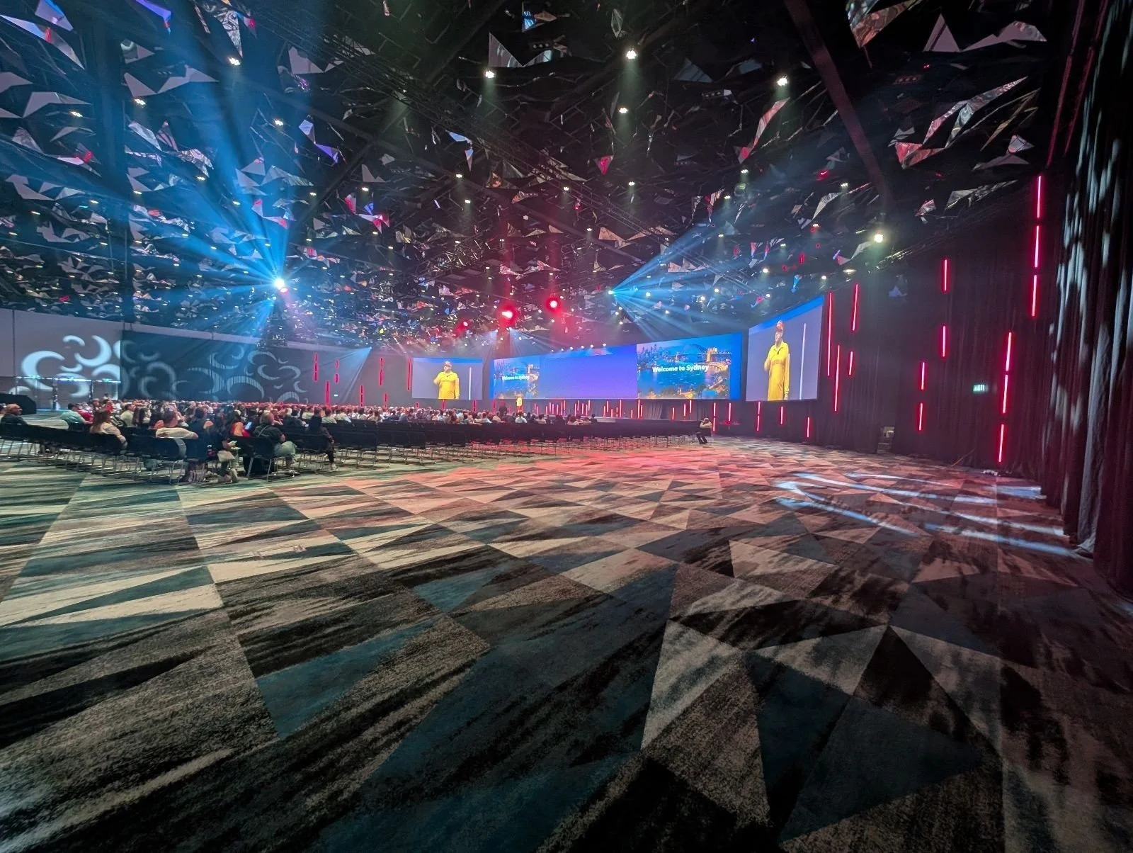 General session for a few thousand attendees: mirrored sculptural ceiling, full IMAG wall and moving light rig