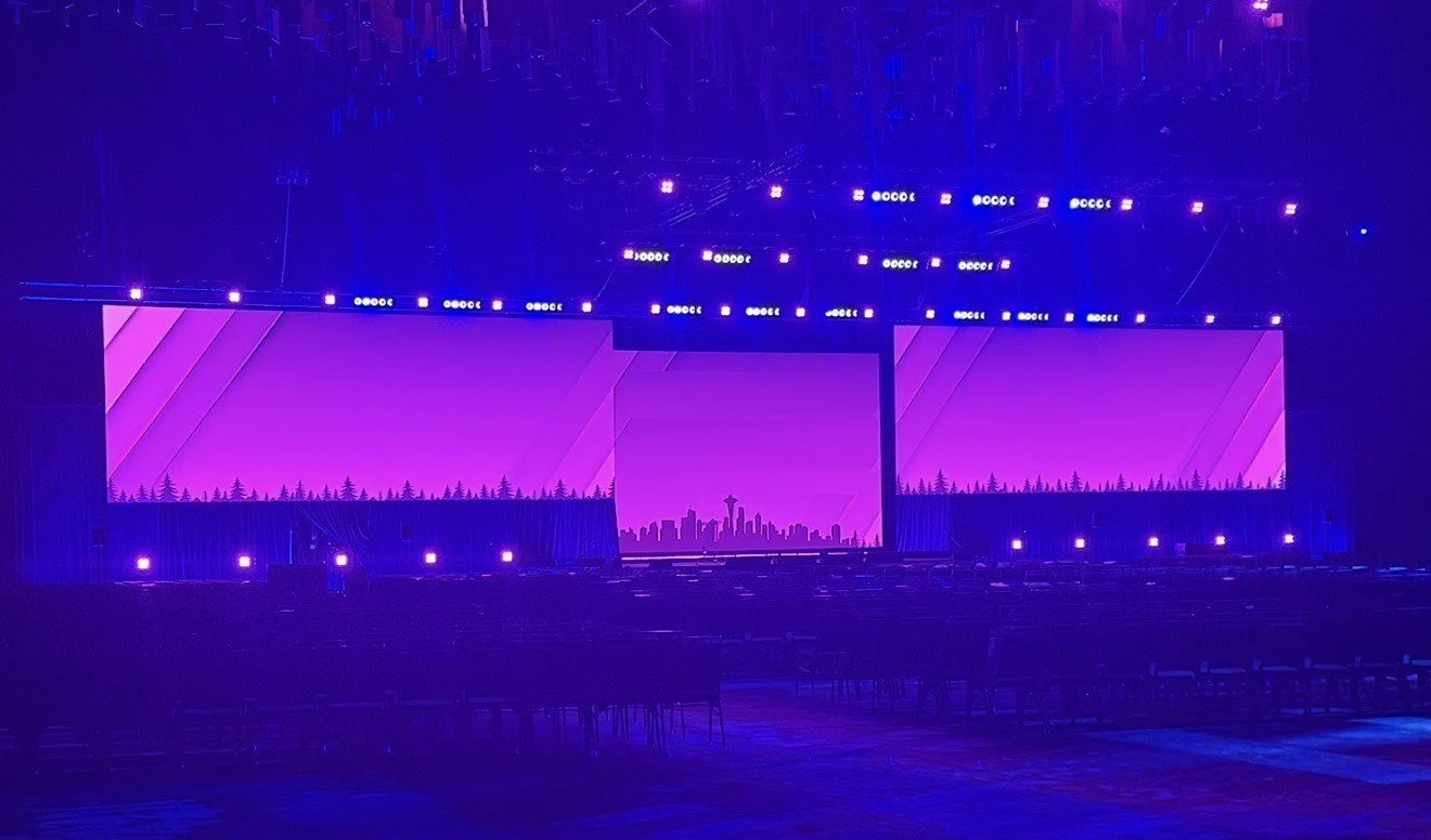 Arena scale general session: wide LED canvas with a custom skyline look and layered truss lighting