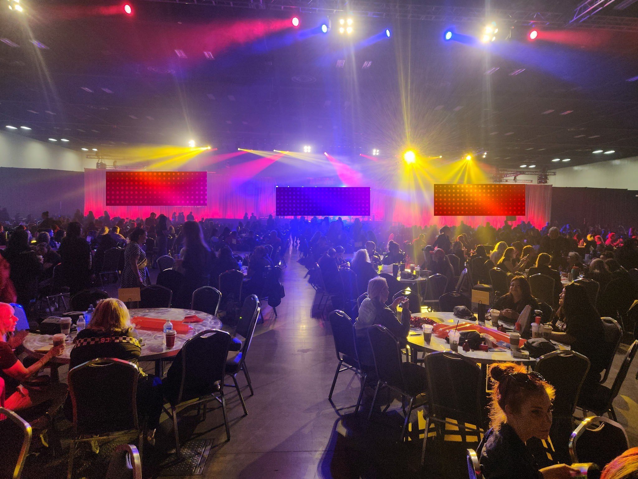 Convention hall rally for thousands: three screen stage, red drape surround and a full moving light show