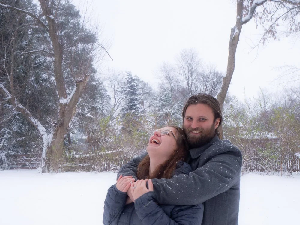 Engaged woman laughing while being hugged by a man in the snow