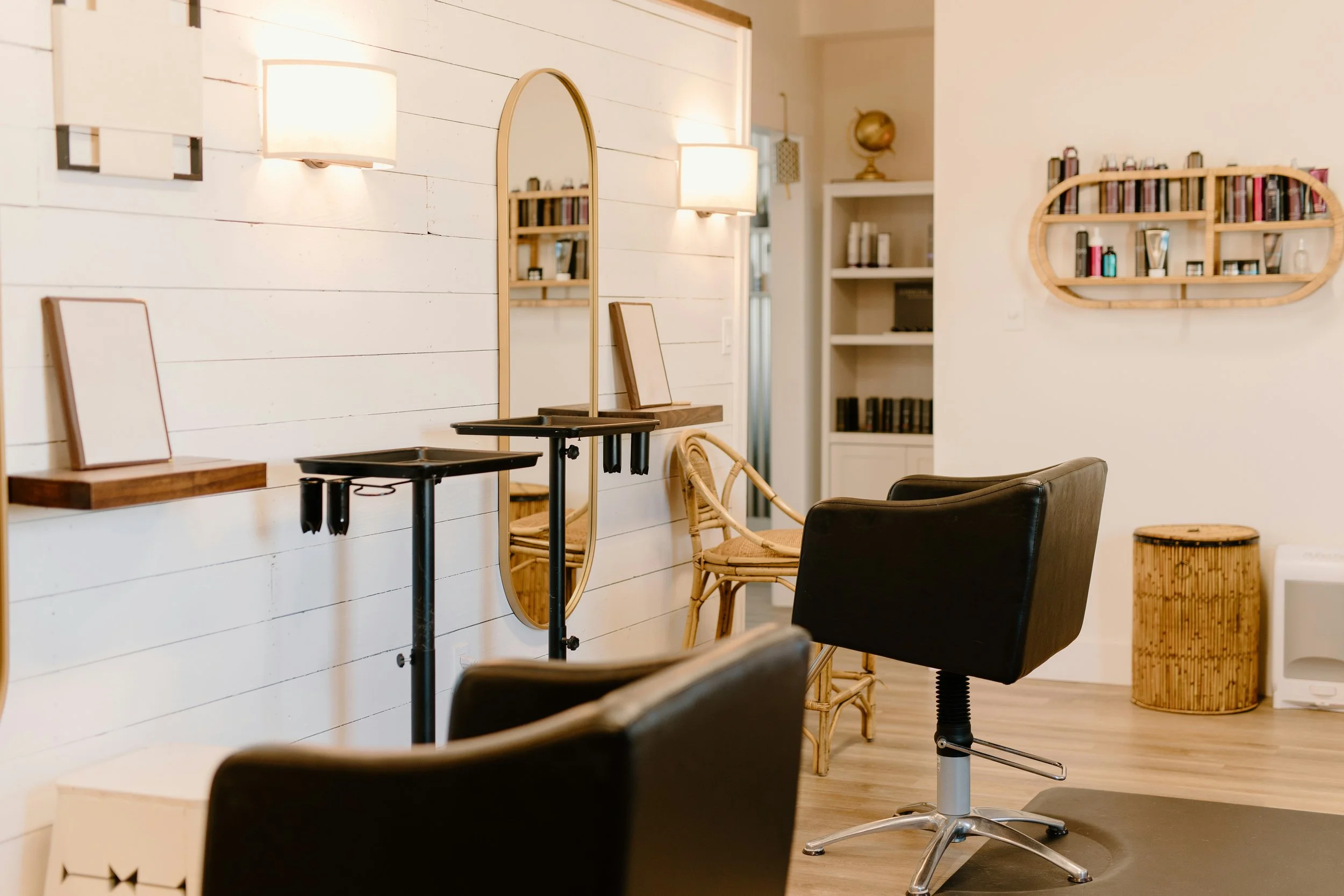 Interior of a room with white shiplap walls, featuring black chairs, wood accents, a mirror, and wall-mounted lights, with shelves and decorative items.