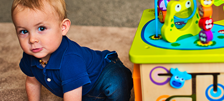 Baby crawling on carpet beside a colorful children's play table with various toys.