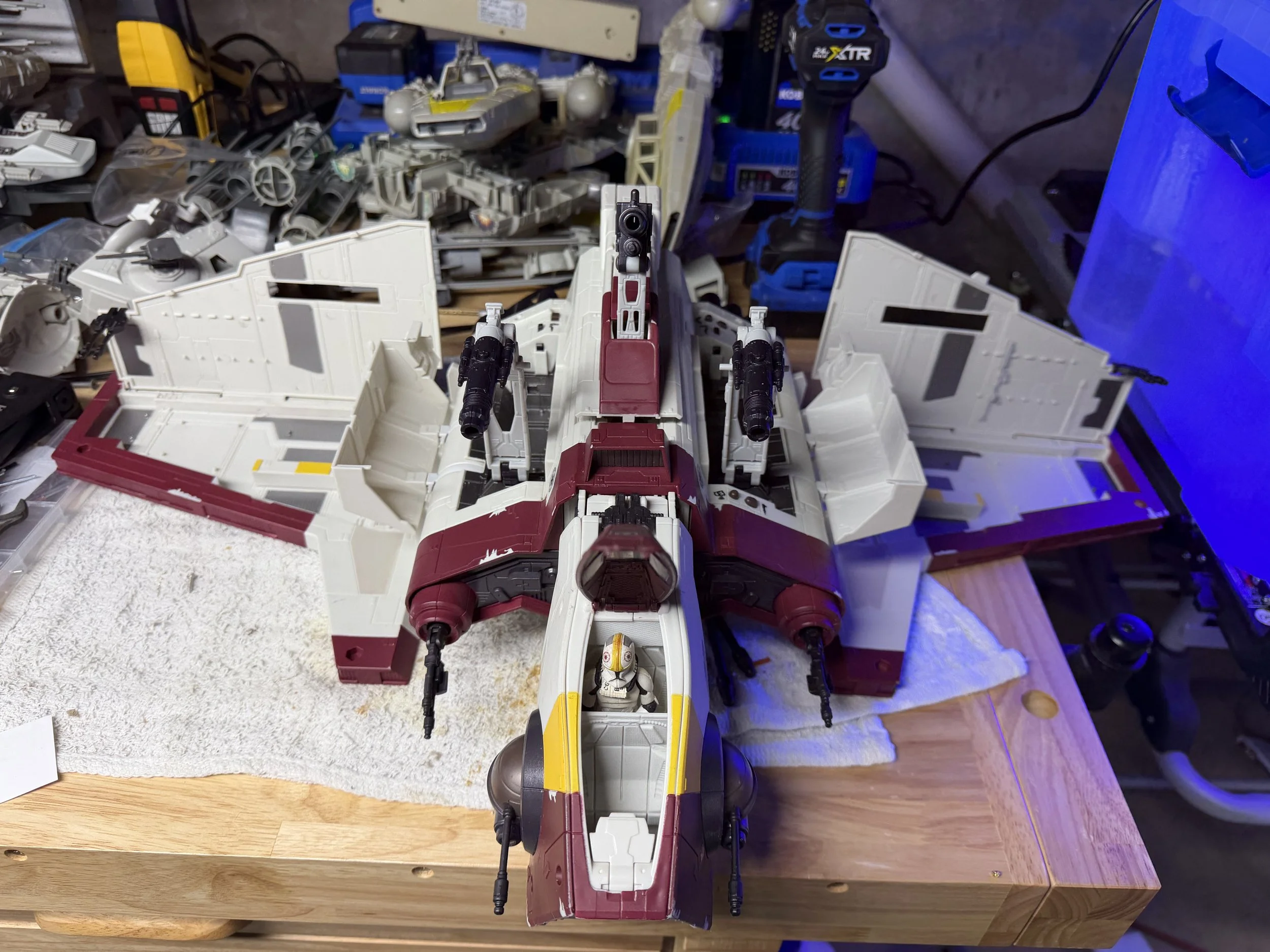 A LEGO Star Wars model of an X-Wing starfighter constructed from white, red, yellow, and black bricks, placed on a wooden table among various tools and parts.