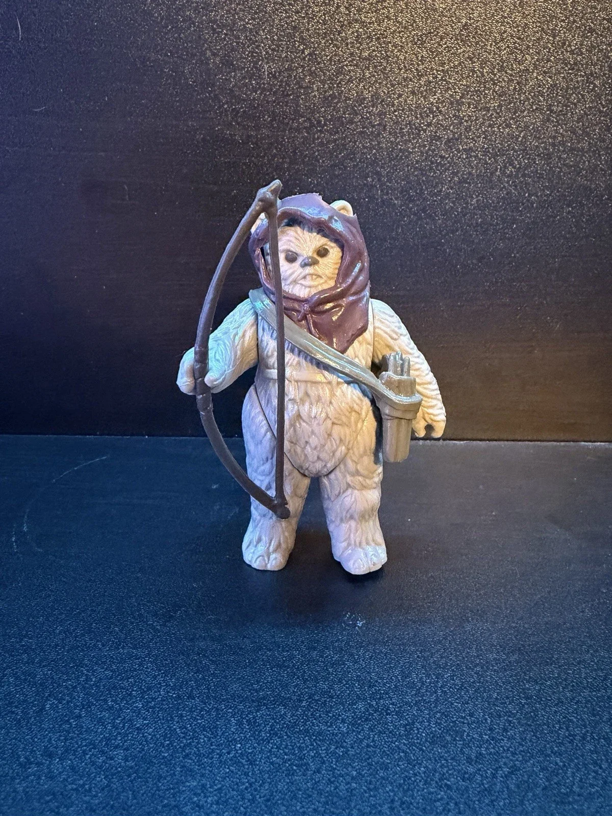 A toy figure of an Ewok from Star Wars holding a bow and a small spear against a dark background.