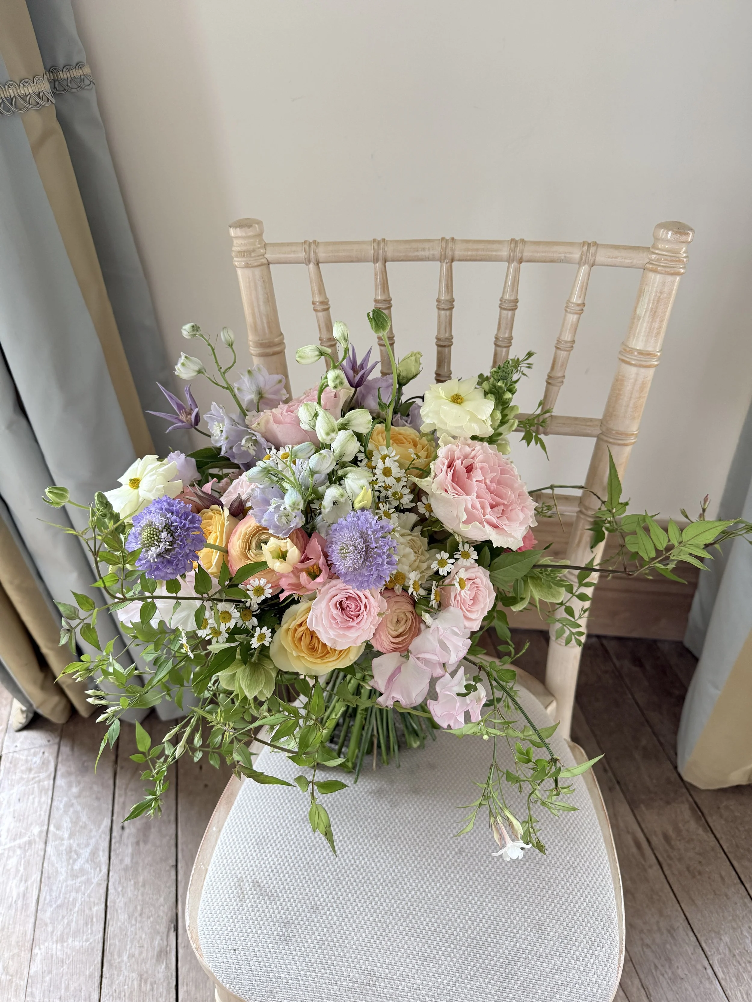 Late Spring, pastels featuring scented Roses, Delphiniums, Ranunculus and Sweet Peas finished with trailing Jasmine