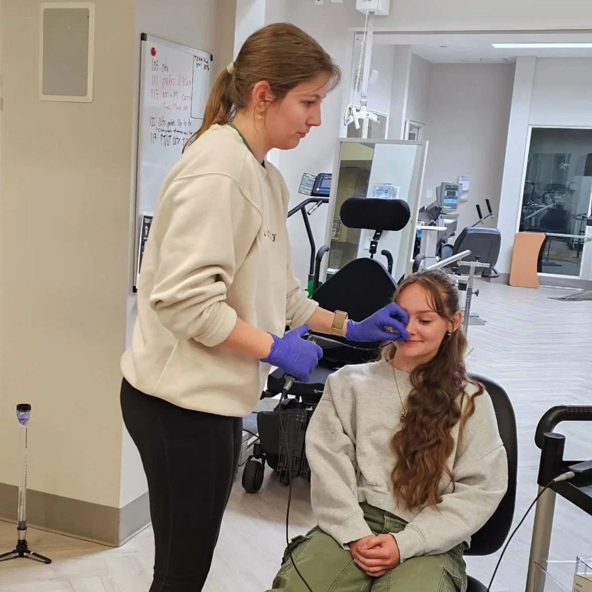 A young female healthcare worker with gloves pressuring the arm of a seated girl with long wavy hair, in a medical facility.