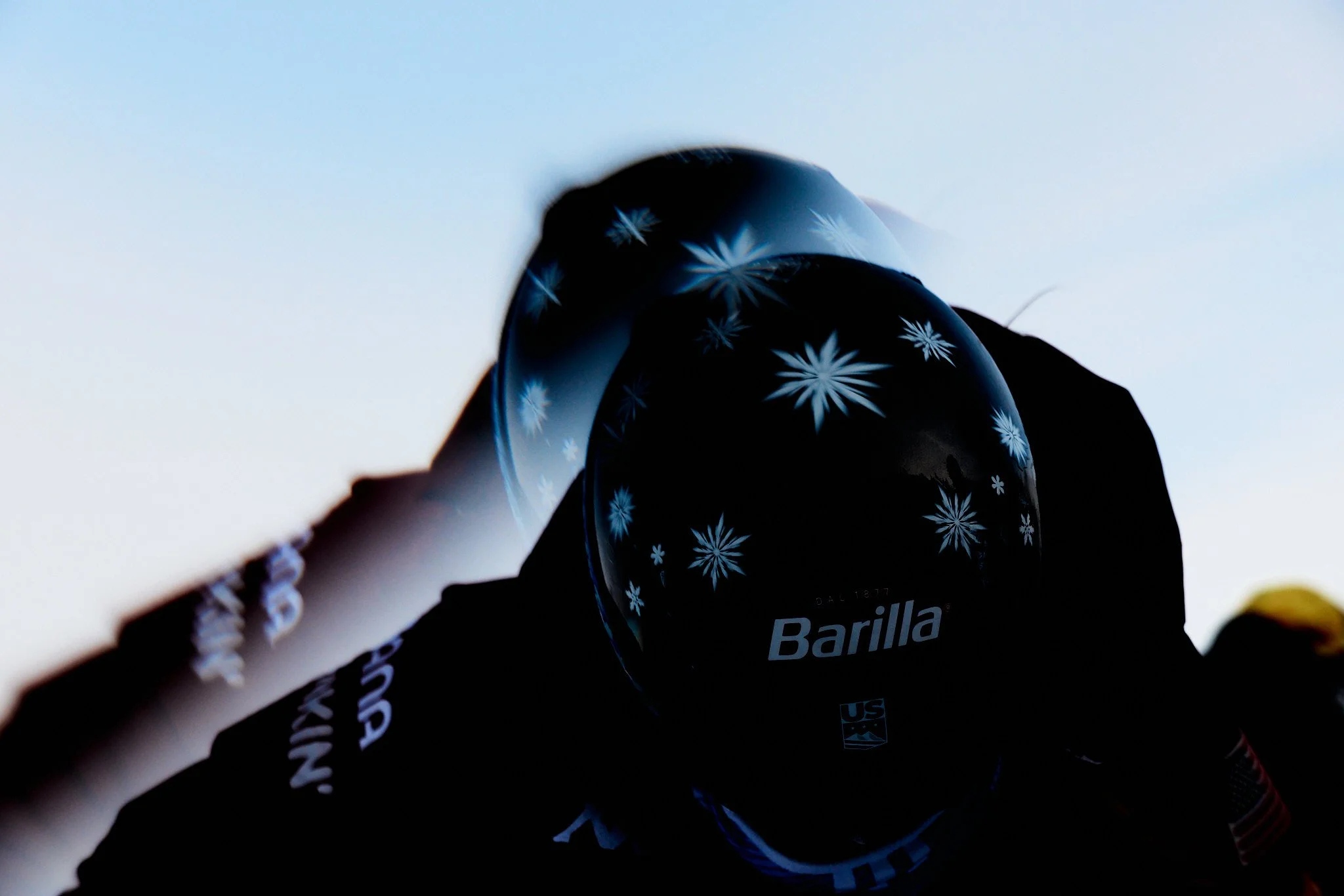 A black balloon with white snowflake patterns and the word 'Barilla' written on it, held by a person against a blue sky background.