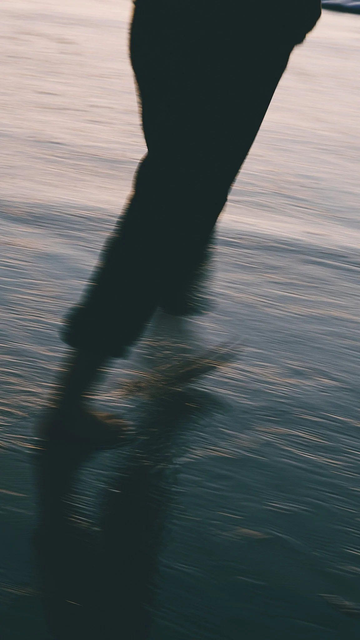 Close-up of a person's legs walking on a sandy beach at sunset.