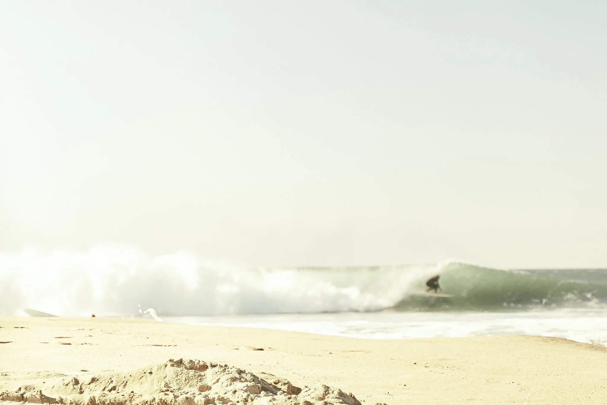 A sandy beach with waves crashing and a large storm or hurricane approaching in the background.