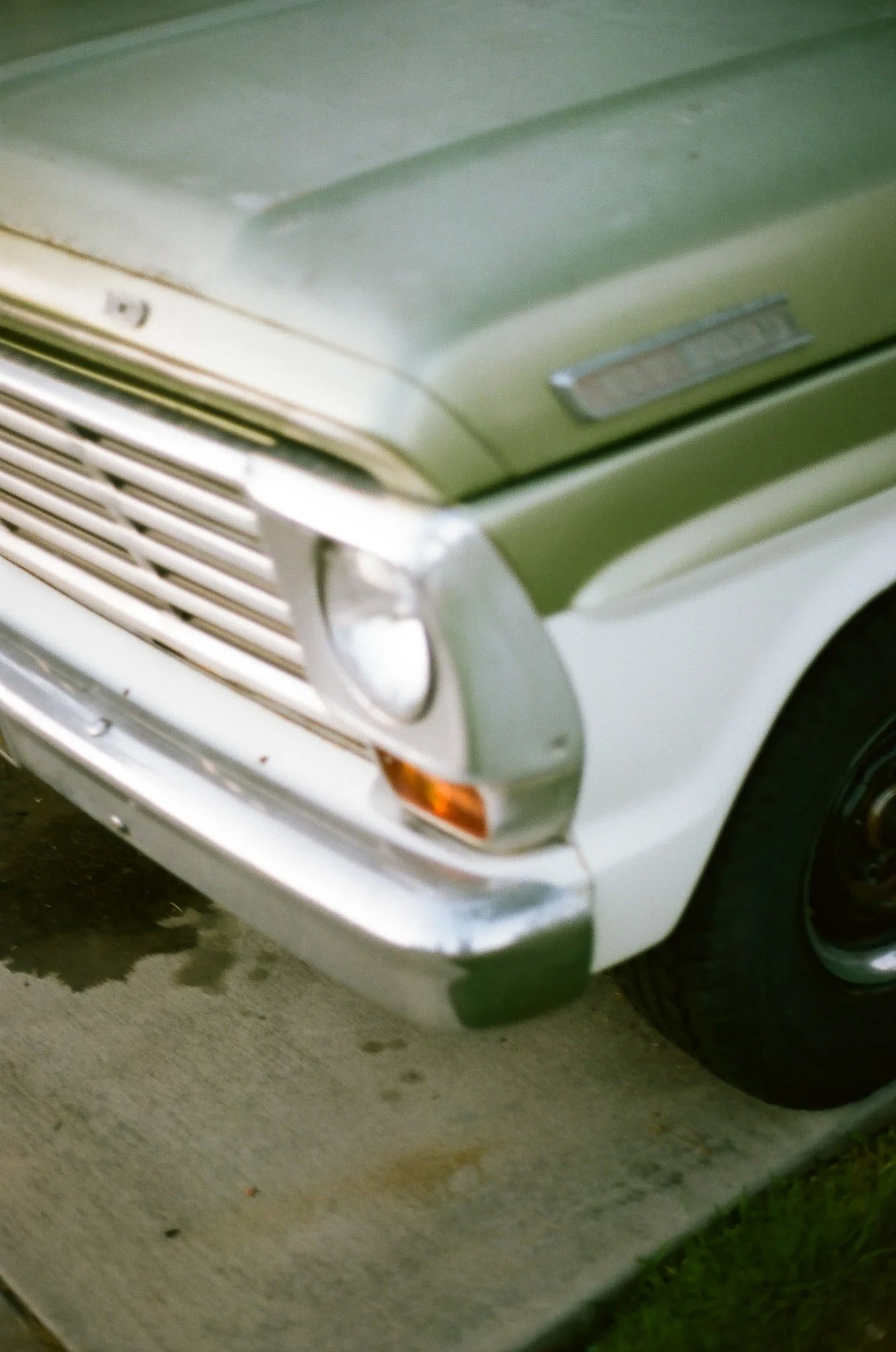 Close-up of the front part of a white vintage car with a grill, headlight, and bumper, parked on a concrete surface.