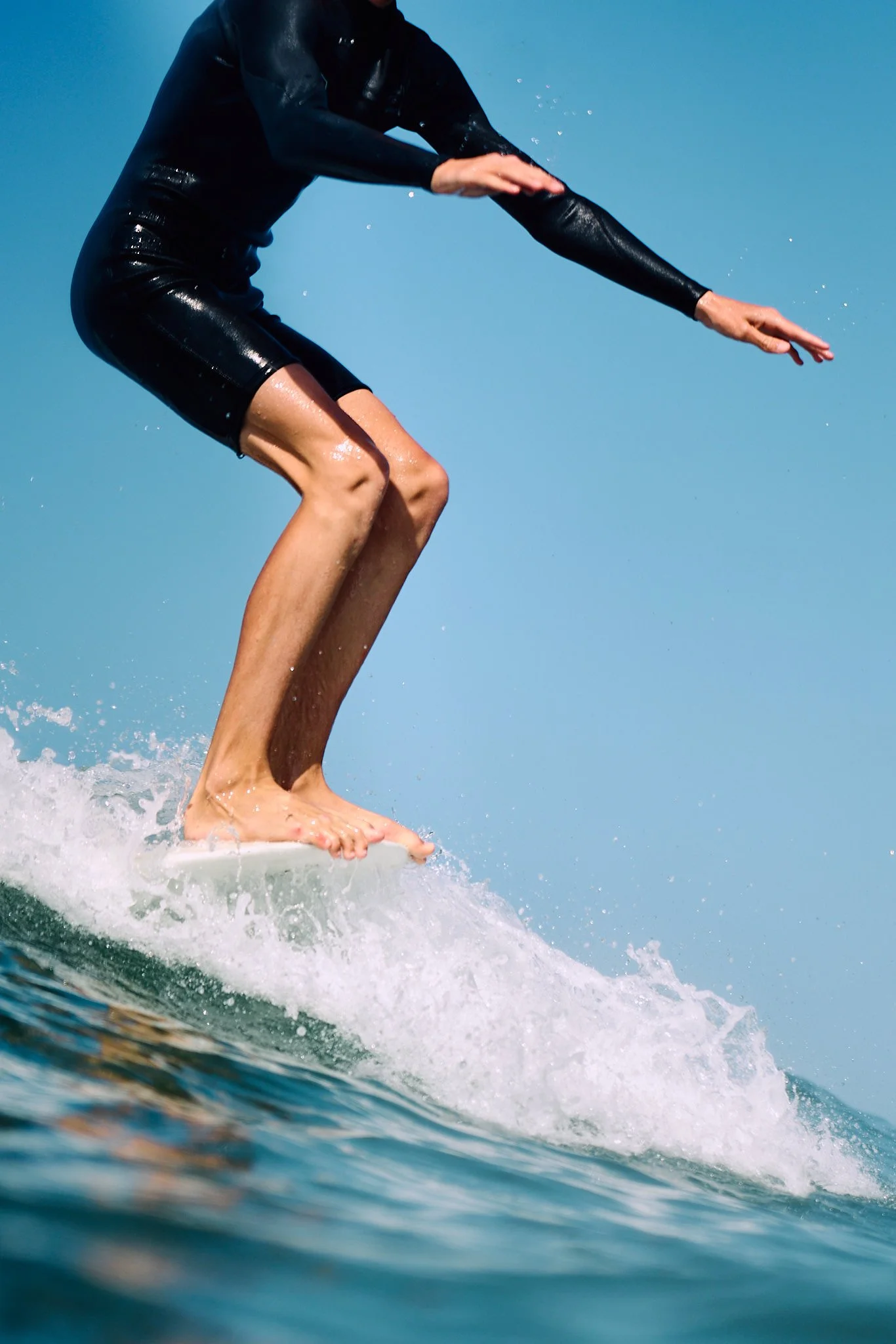 A person wearing a black wetsuit surfing on a blue ocean wave.