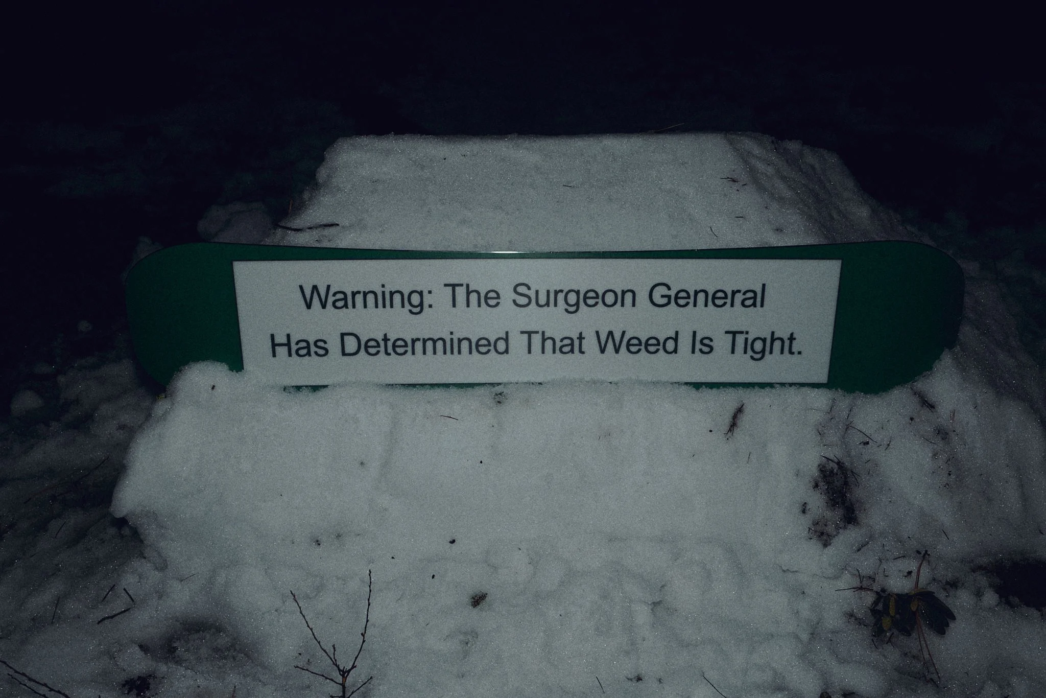 A warning sign placed on snow indicates that the weed is tight, with snow and some small twigs around it.