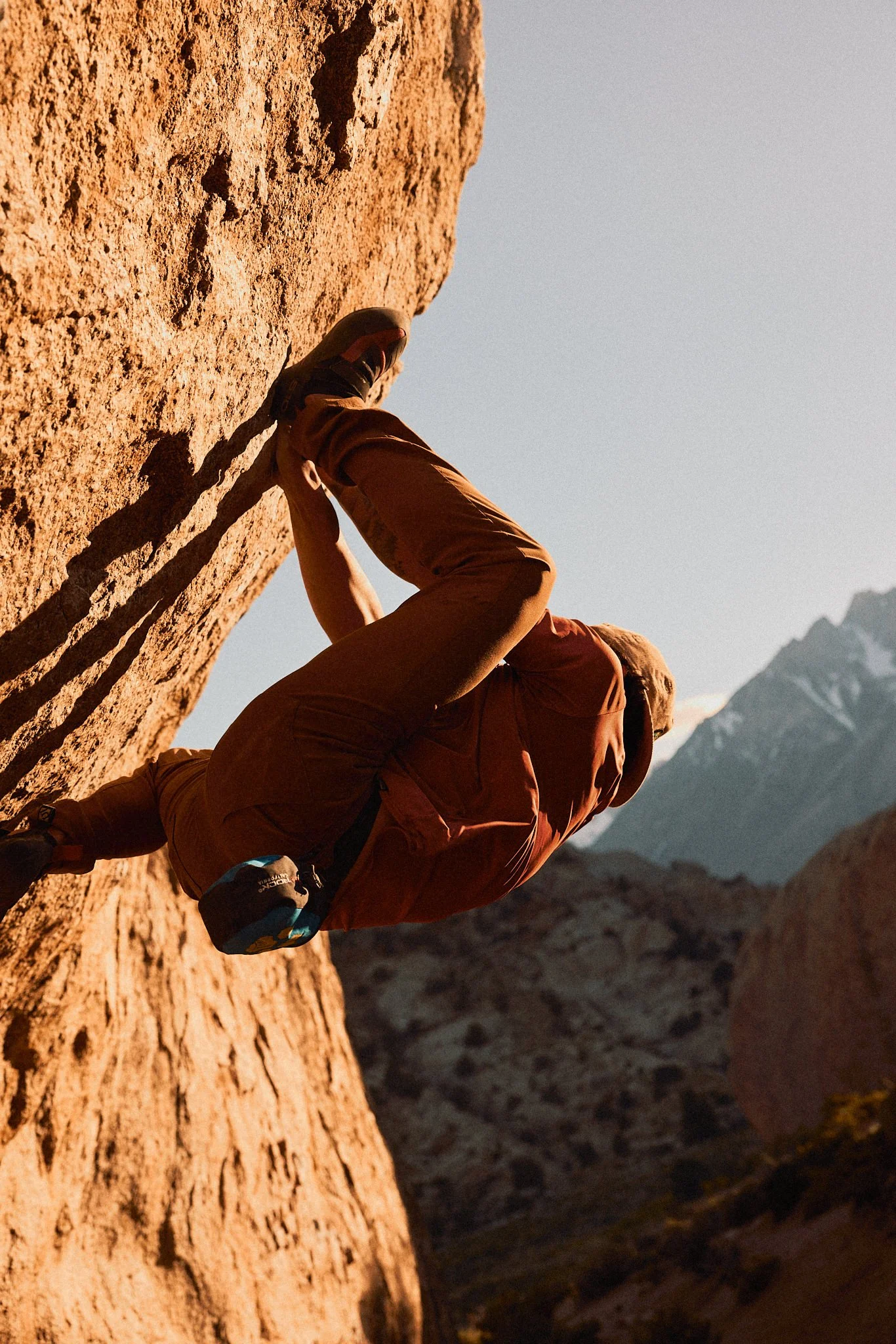 A person rock climbing on a steep red rock face in a mountainous desert landscape.