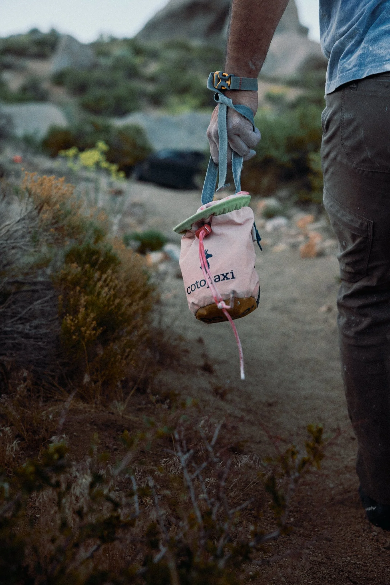 Person holding a pink and green item labeled 'coto taxi' in a rocky outdoor environment.