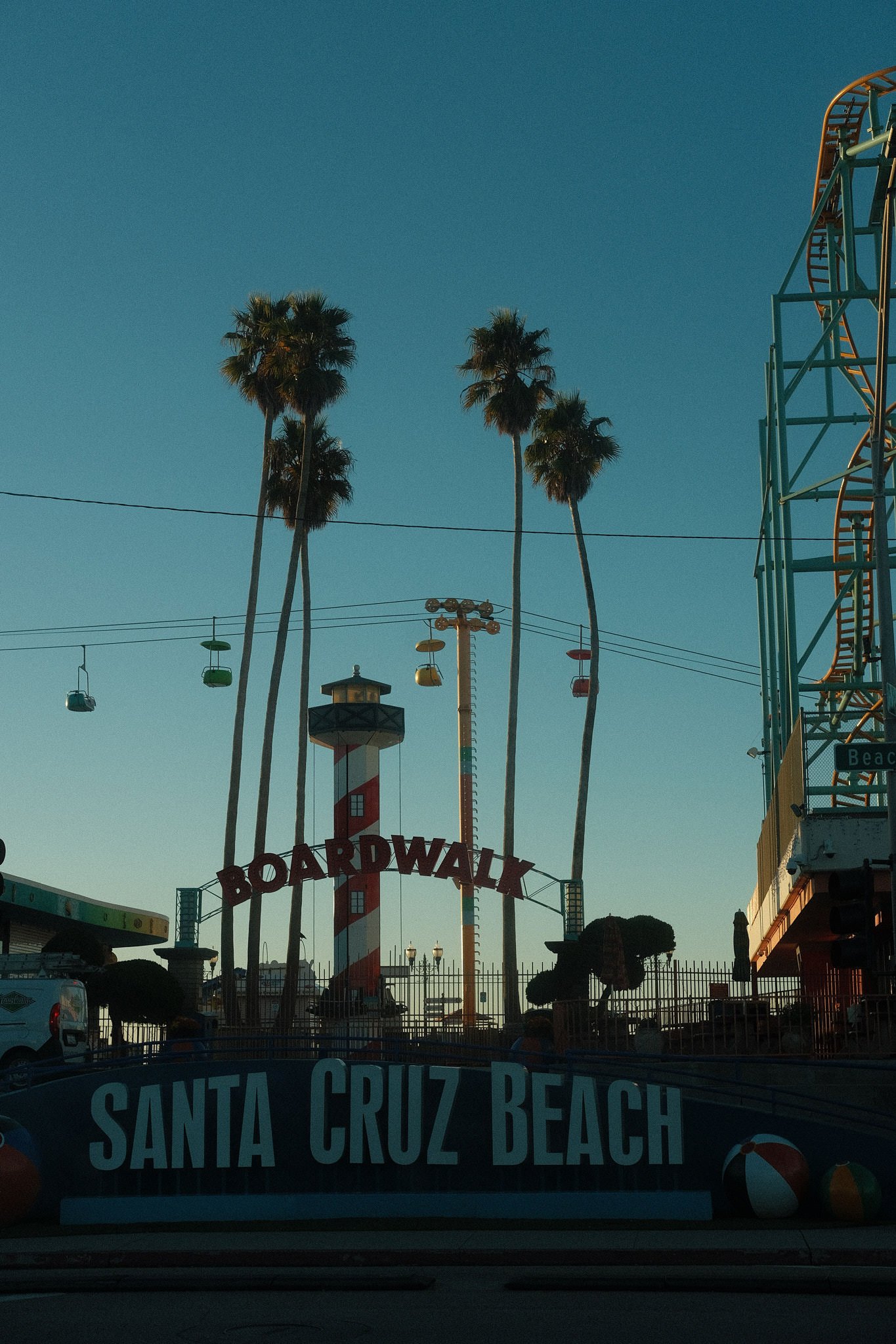 Famous Santa Cruz Beach Boardwalk entrance with tall palm trees, colorful gondola ride, and amusement park rides visible in the background during daytime.