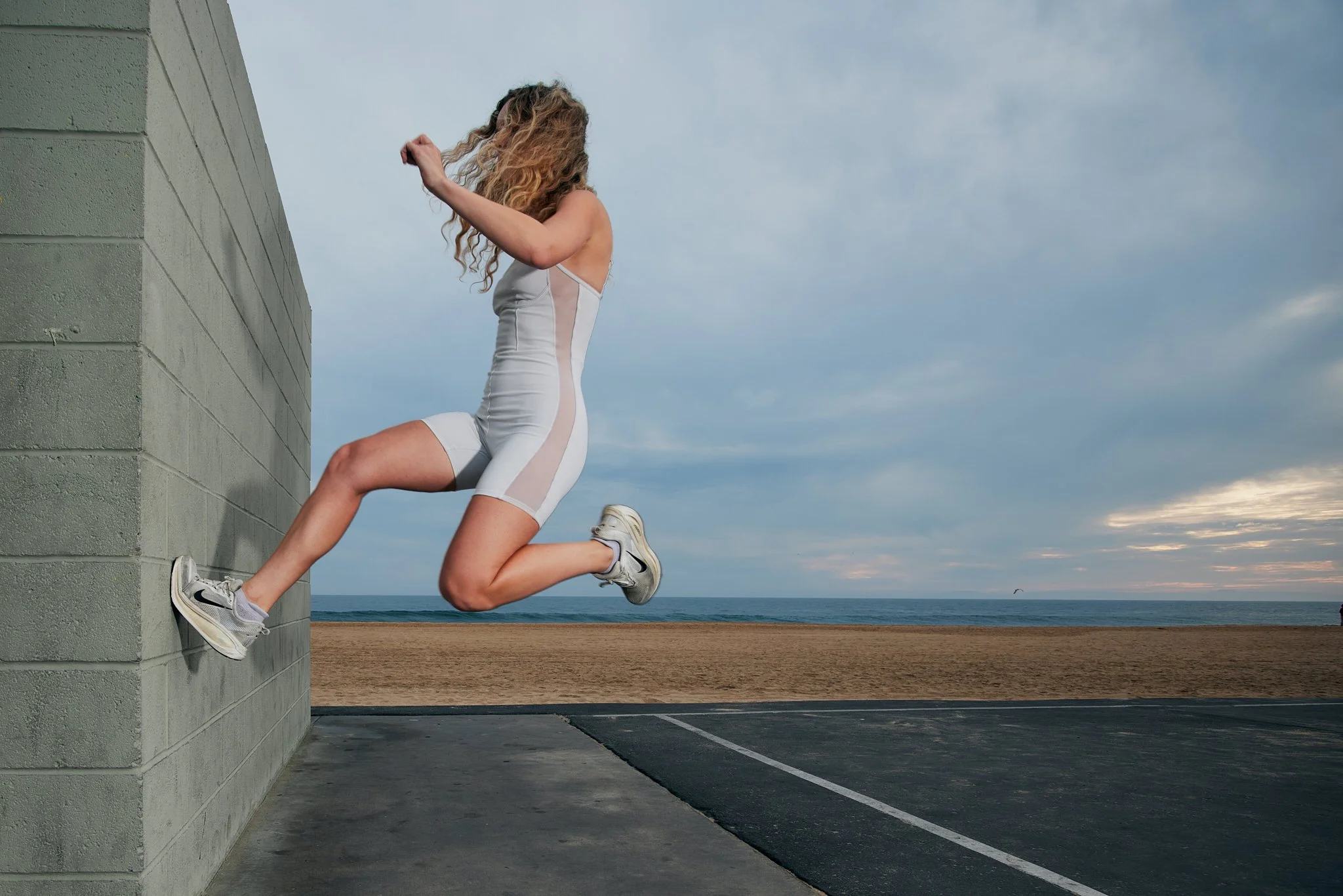 Female athlete climbing a concrete wall outdoors near the beach during cloudy weather.