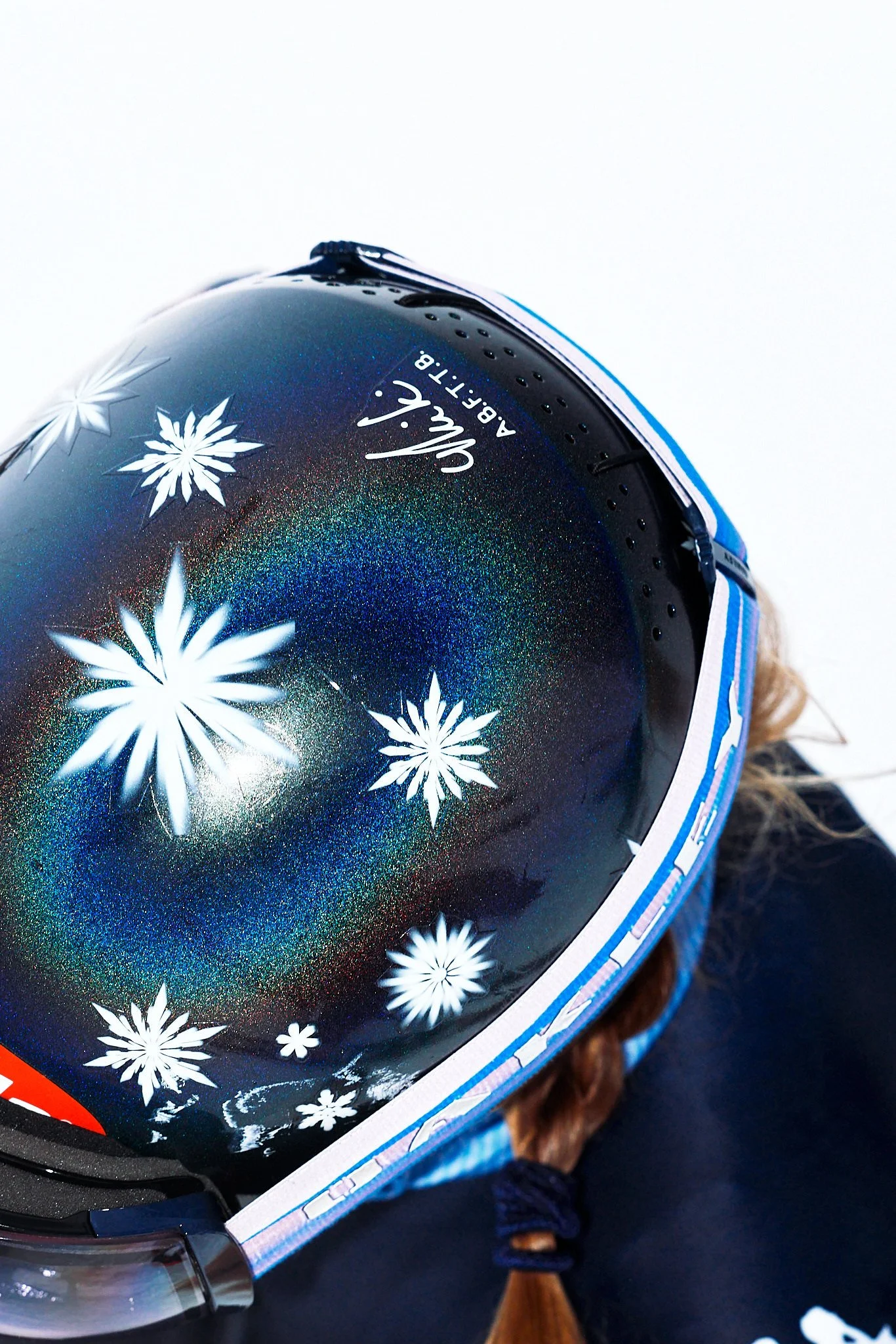 Close-up of a snowflake-themed helmet with a shiny, holographic finish, featuring snowflake illustrations and the brand name 'Kelly Abbott' on a white background.