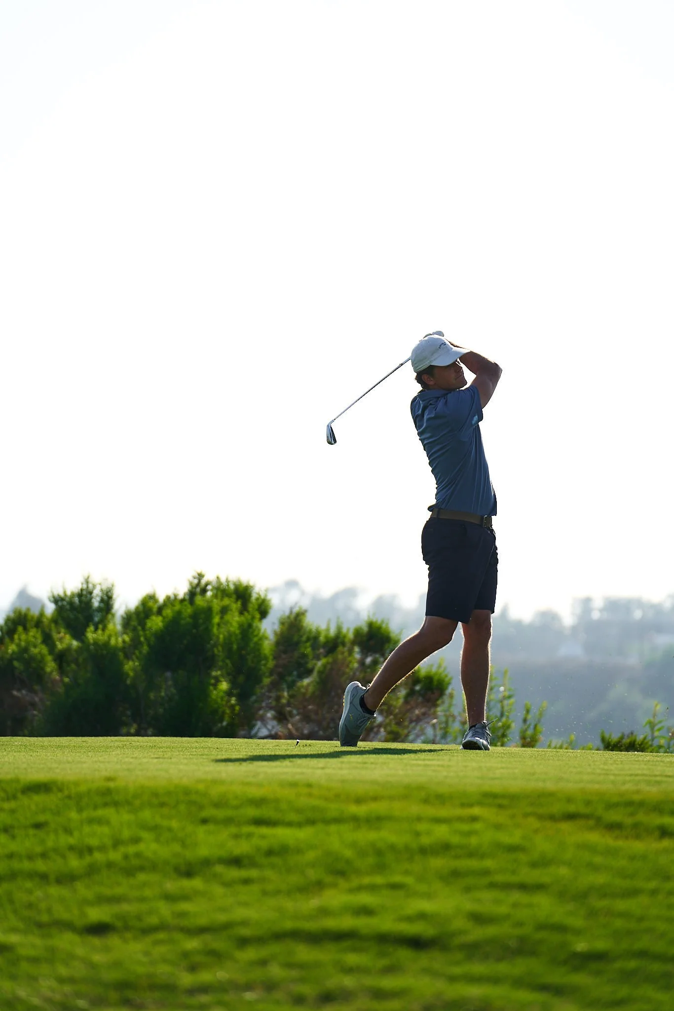 A man playing golf on a sunny day, swinging a golf club on the green grass.