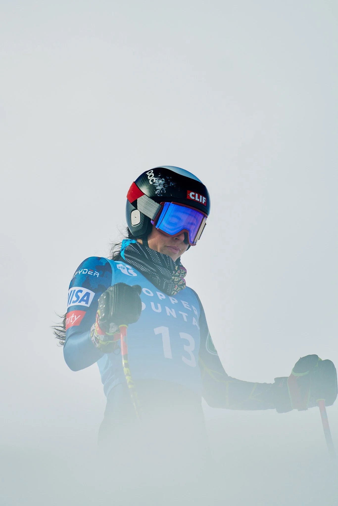 A skier wearing a helmet, goggles, and a blue racing jersey with the words 'Super Utah' and the number 13, holding ski poles against a foggy or overcast sky.