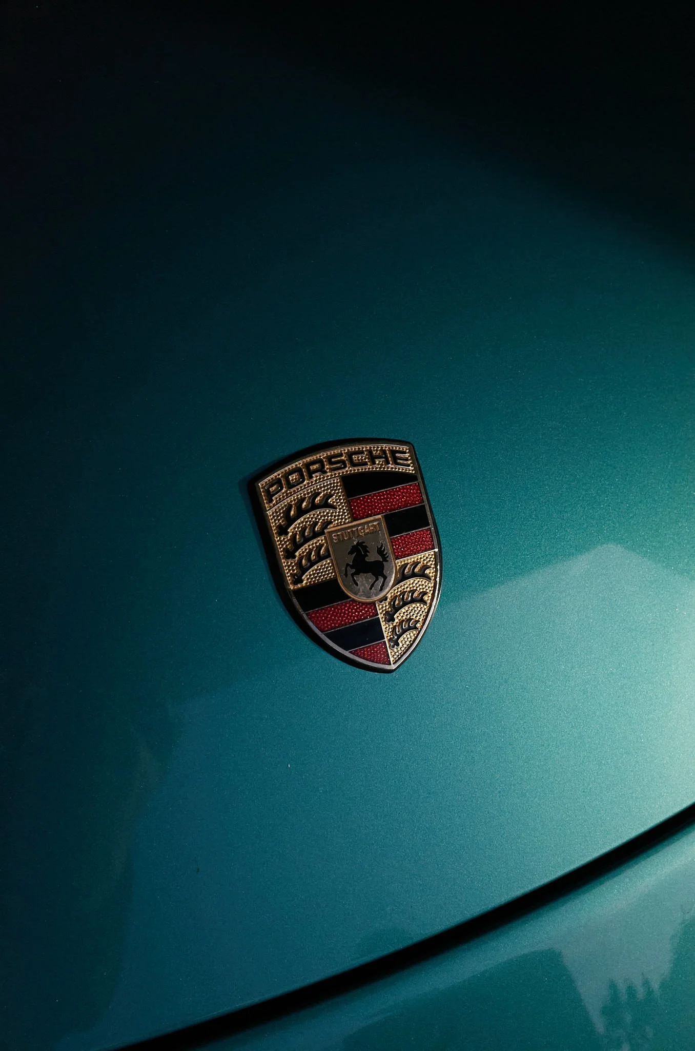 Close-up of a teal Porsche car with a Porsche emblem on the hood.