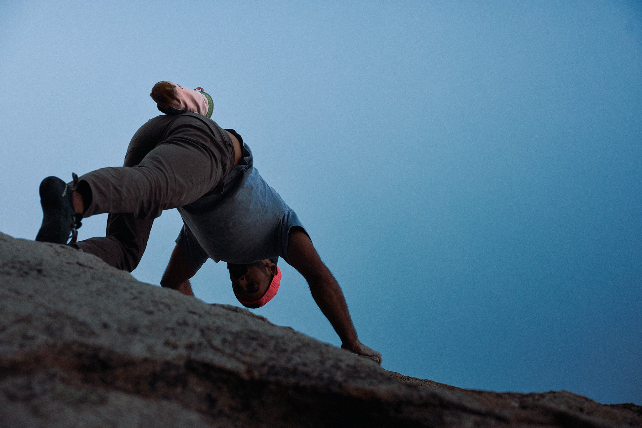 A person in athletic gear, including a pink hat, climbing on a rocky surface against a twilight sky.