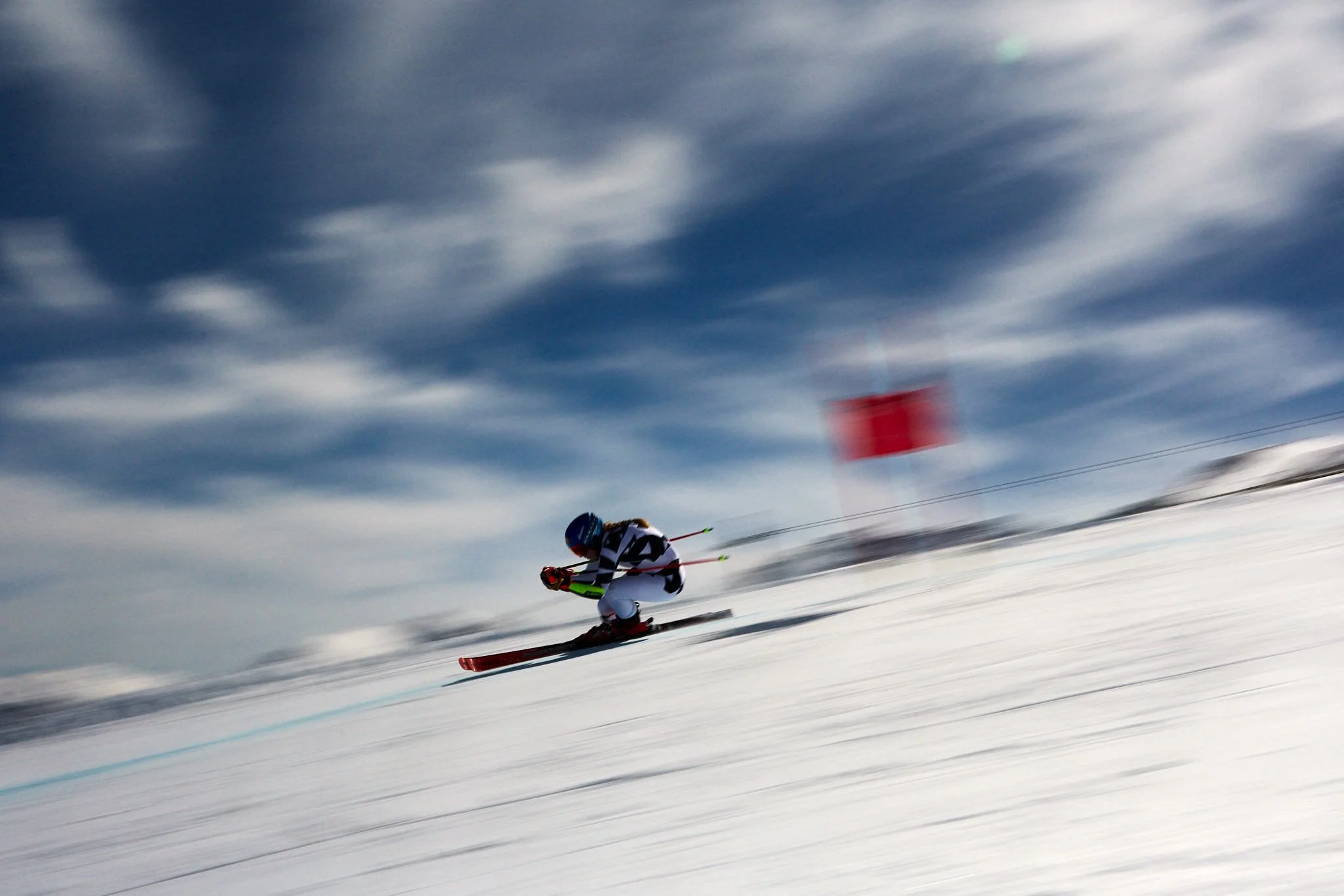 A skier in a racing suit and helmet skiing downhill on a snow-covered slope under a cloudy sky.