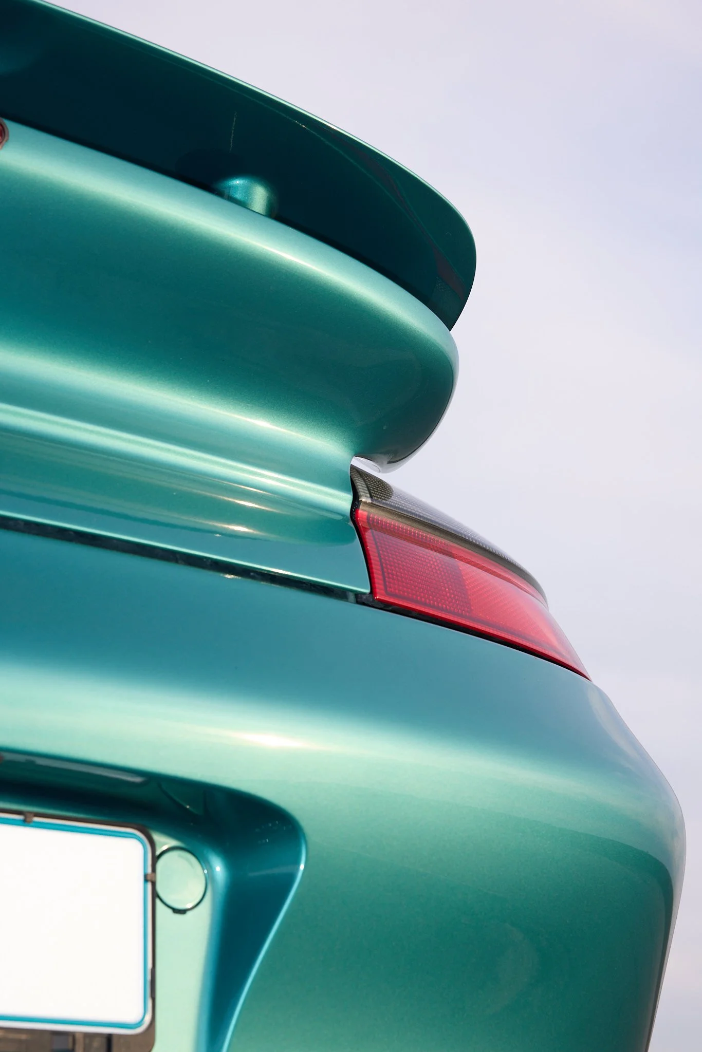 Close-up of the rear end of a vintage turquoise car, showing part of the taillight, trunk, and a luggage rack.