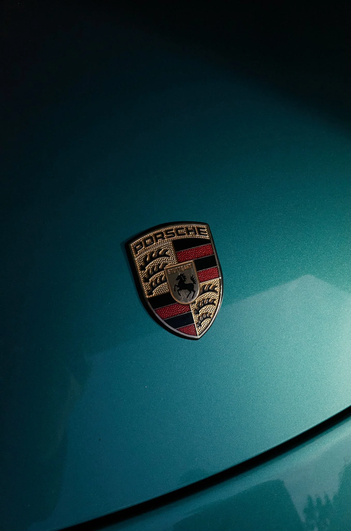 Close-up of a Porsche logo on a teal-colored car.