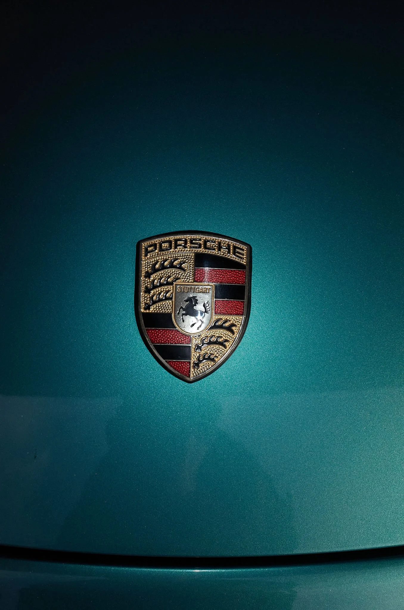Close-up of a Porsche car emblem on a teal-colored vehicle.