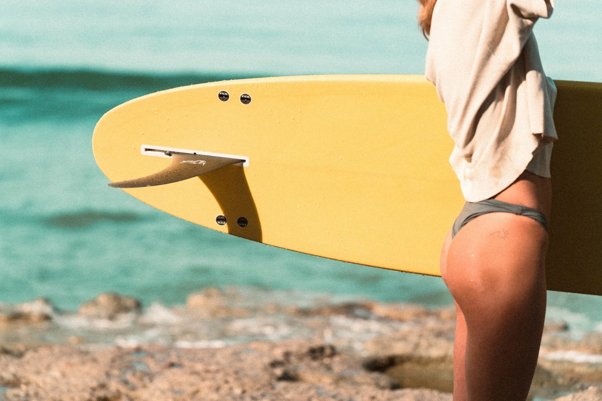 A woman carrying a yellow surfboard walking along a sandy beach near the water.