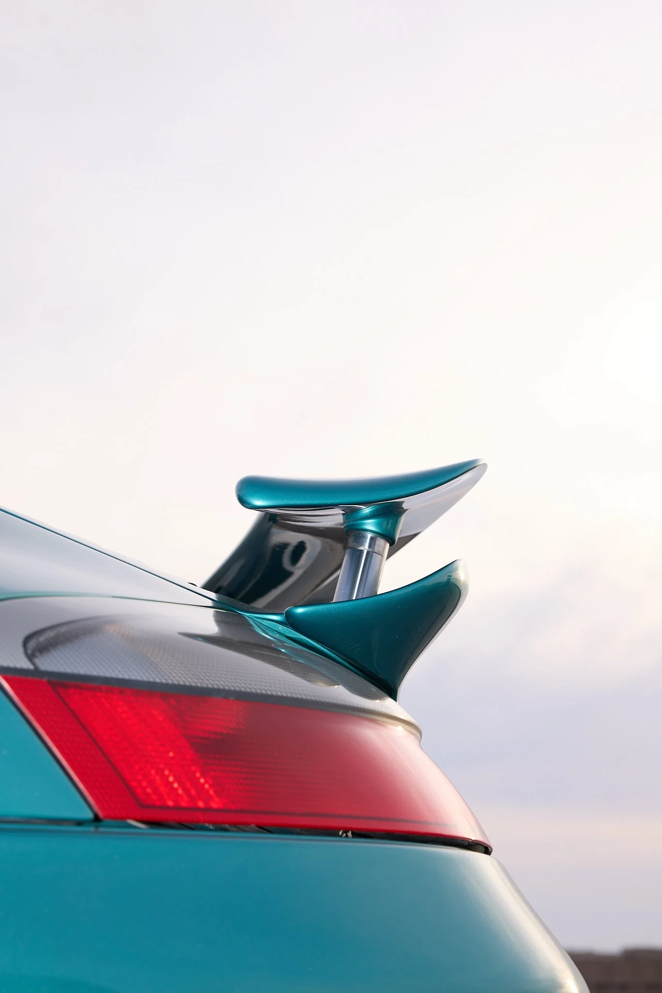 Close-up of the rear section of a modern electric car, showing the taillight, rear wing, and part of the roof against a cloudy sky.