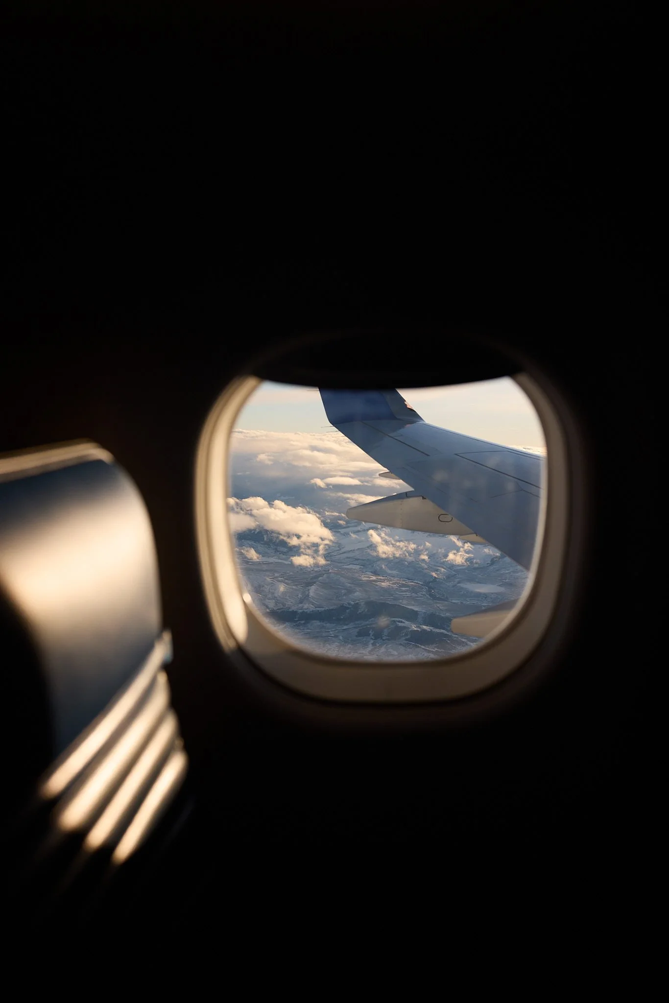 View from an airplane window showing the wing and clouds below during daytime flight.