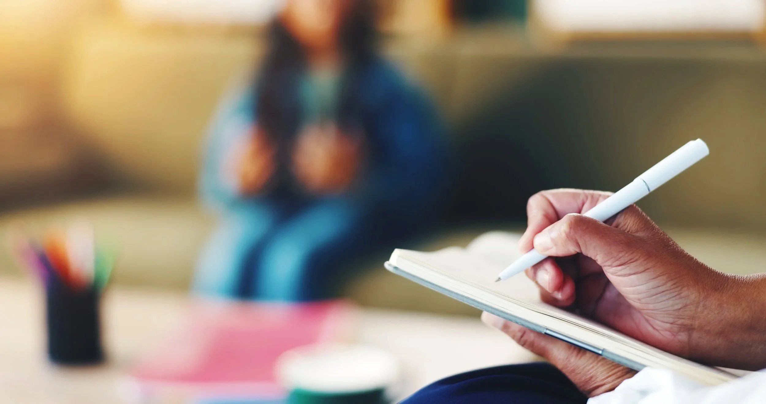Hand of counselor writing in notebook with child out of focus in background