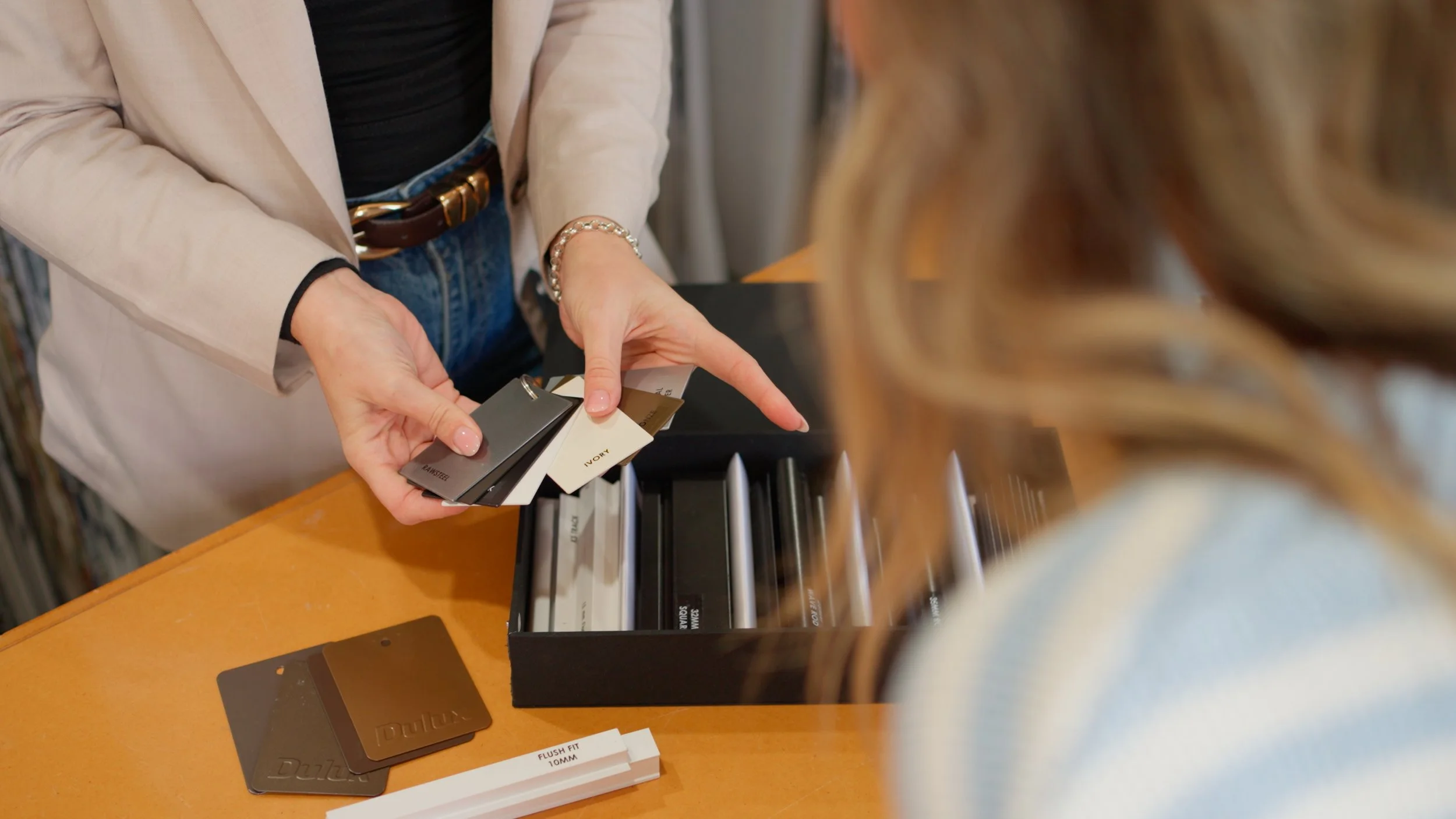 A person holding color swatches in a store, with a display of paint color samples and color cards on the counter.